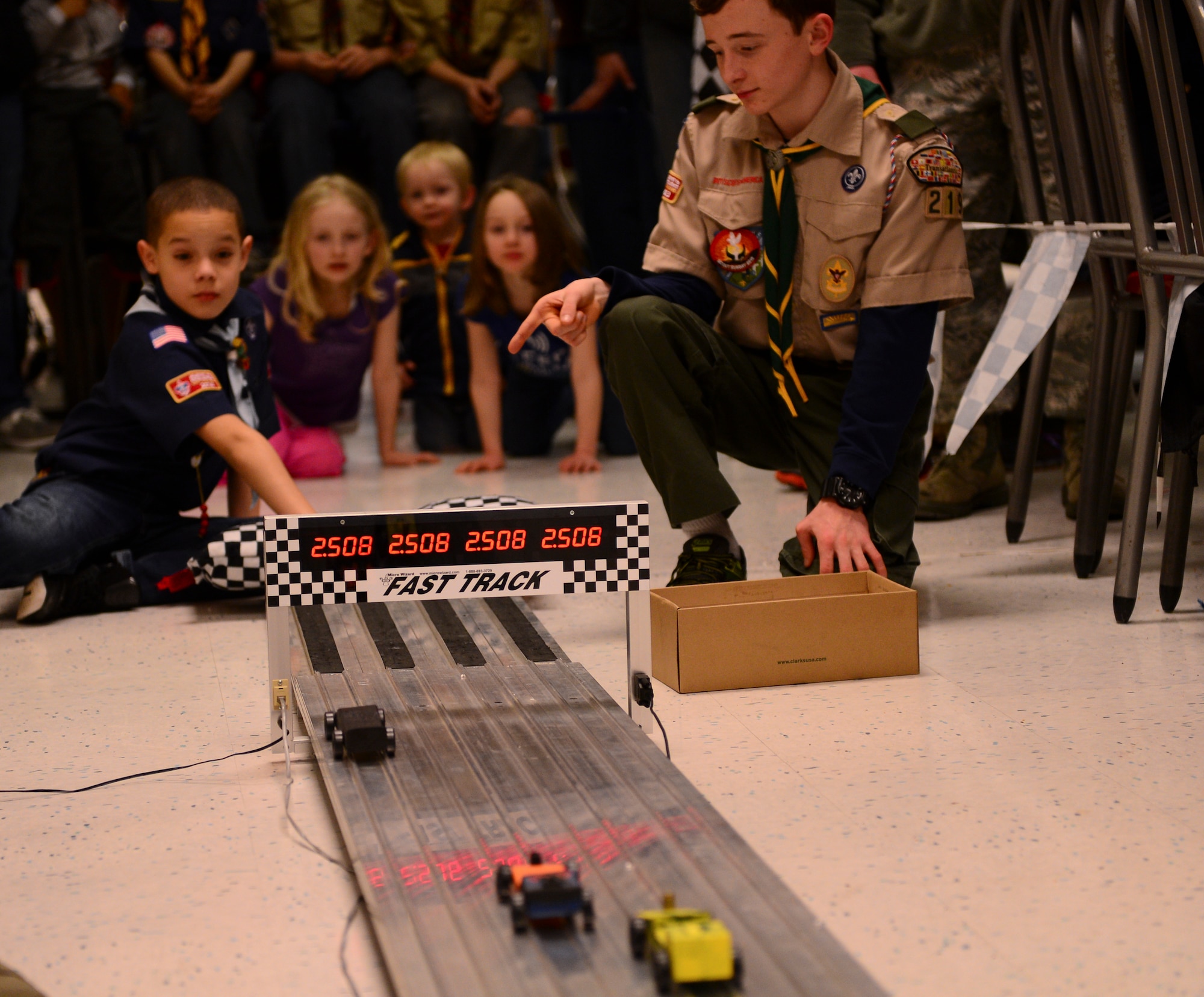 Children watch as boxcars finish during the annual Cub Scout Pack 219 Pinewood Derby at the Exchange on Royal Air Force Lakenheath, England, Feb. 24, 2015. All cars were made from a seven-inch piece of wood and had to be under the Boy Scouts of America-regulated five ounces to participate. (U.S. Air Force photo by Senior Airman Nigel Sandridge/Released)