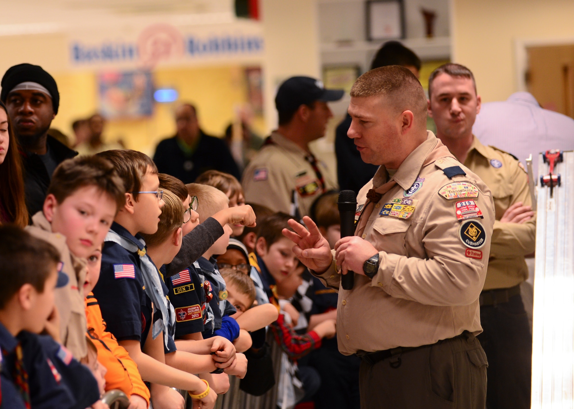 Capt. Zackery Kalinauskas, 48th Medical Group disease manager and Cub Scout Pack 219 Cubmaster, gains the attention of an audience at the pack’s annual Pinewood Derby at the Exchange on Royal Air Force Lakenheath, England, Feb. 24, 2015. The Pinewood Derby is an event in which members of the scouts race handcrafted cars carved from wood. (U.S. Air Force photo by Senior Airman Nigel Sandridge/Released)