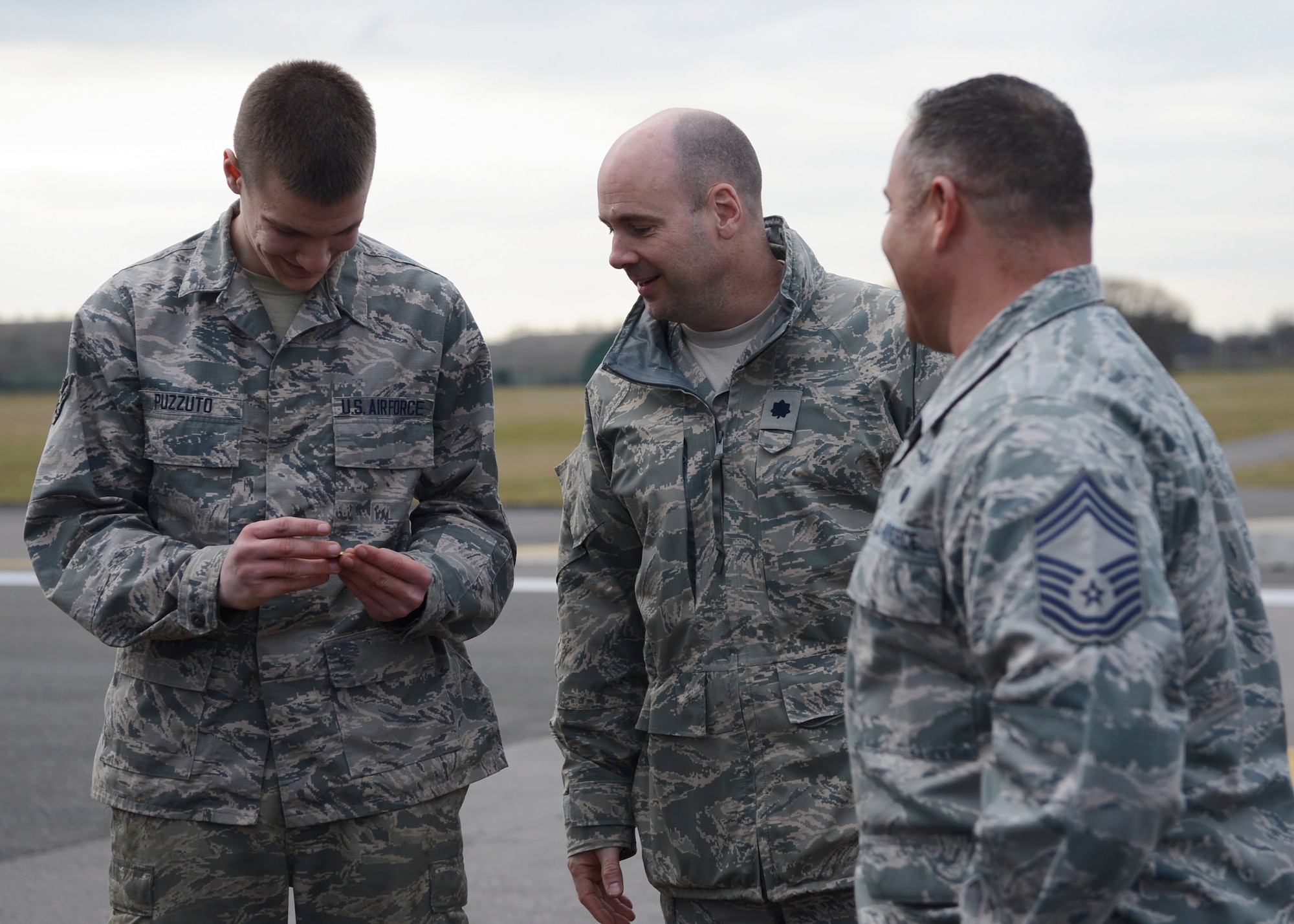 Airman 1st Class Jake Puzzuto, 48th Civil Engineer Squadron heavy equipment operator, shows his achievement coin to Lt. Col. Connor Blackwood, 48th Mission Support Group deputy commander, and Chief Master Sgt. Brian Kentta, 48th MSG superintendent, Feb. 25, 2015 at Royal Air Force Lakenheath, England. He was coined for his hard work repairing a pothole on the flightline that could have cost the 48th Fighter Wing millions of dollars by diverting air traffic. (U.S. Air Force photo by Airman 1st Class Dawn M. Weber/Released)