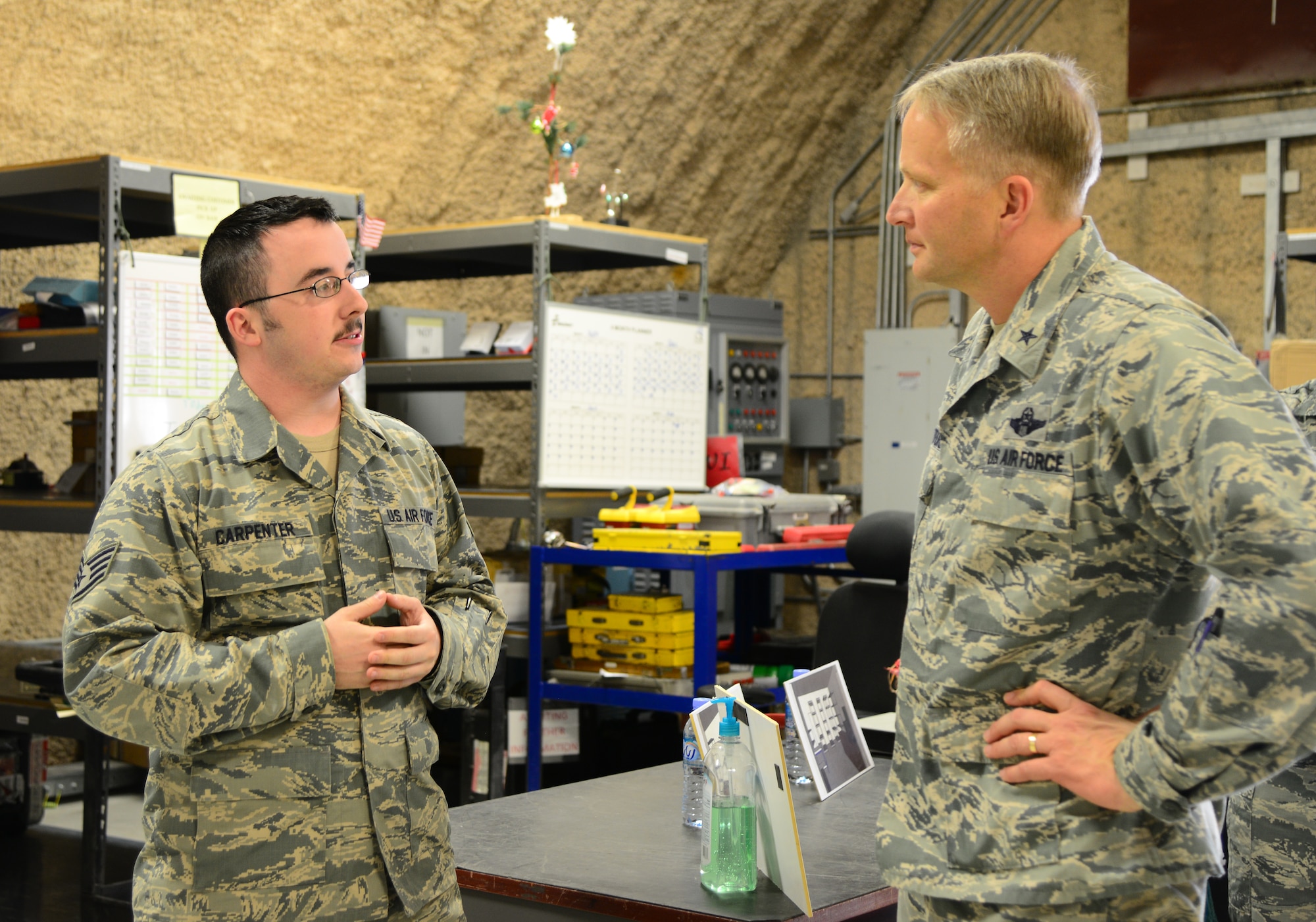 U.S. Air Force Staff Sgt. Paul Carpenter, left, 379th Expeditionary Maintenance Squadron, speaks with Brig. Gen. Darren Hartford, 379th Air Expeditionary Wing commander, Dec. 29, 2014, at Al Udeid Air Base, Qatar. Carpenter, who works in the Precision Measurement Equipment Laboratory, spoke with Hartford about the upgrades the PMEL shop will be receiving after they move into a more robust building. Carpenter is deployed from Travis Air Force Base, Calif. (U.S. Air Force photo by Senior Airman Kia Atkins)