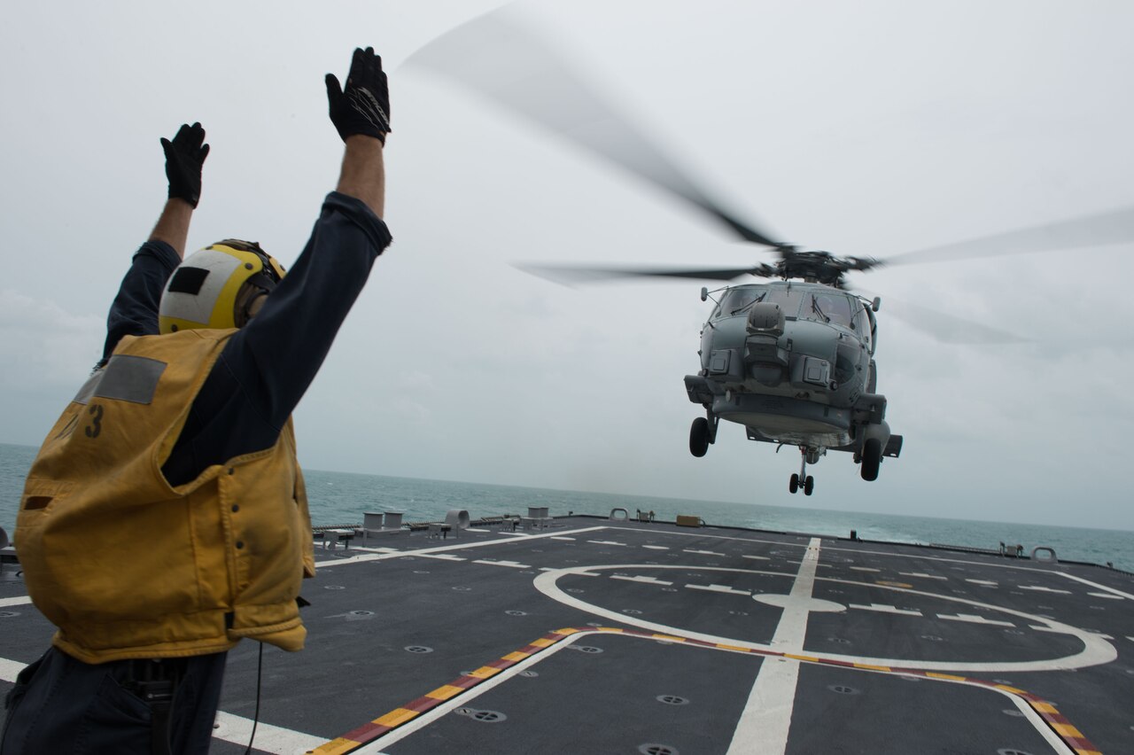 U.S. Navy Petty Officer 2nd Class Adam Garnett signals an MH-60R Sea Hawk helicopter from Helicopter Maritime Strike Squadron 35 on the flight deck of the littoral combat ship USS Fort Worth, Jan. 3, 2015. Fort Worth is currently in the Java Sea conducting helicopter search operations with the USS Sampson as part of Indonesian-led efforts to locate downed AirAsia Flight 8501. U.S. Navy photo by Petty Officer 2nd Class Antonio P. Turretto Ramos