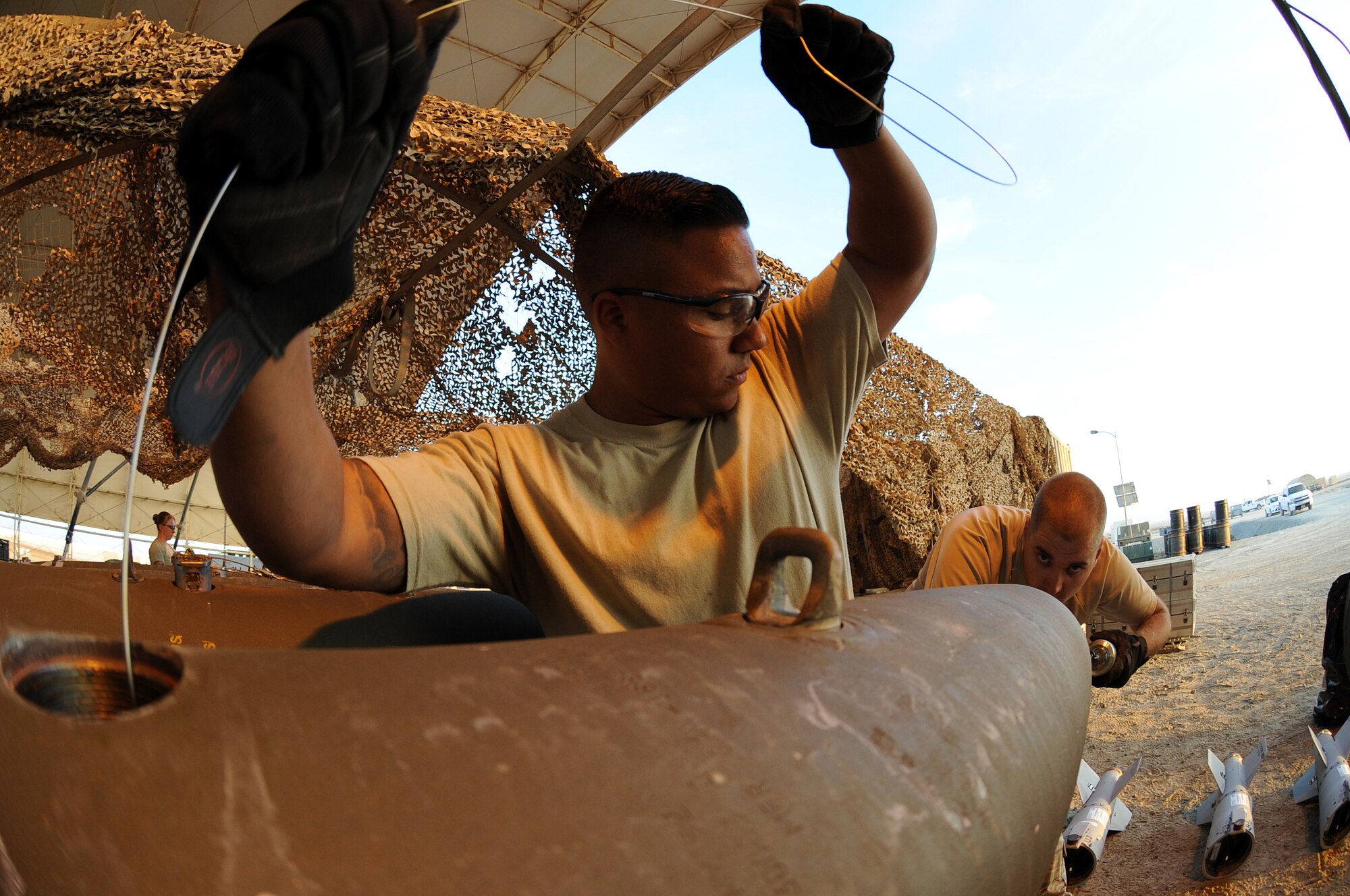 Airman 1st Class Luis assists Senior Airman Adam with feeding a power cable into a MK-82 bomb conduit Dec. 21, 2014, in Southwest Asia.  This process is needed to ensure the electrical current generated by the FZU-55 bomb initiator will be fed to the fuze.  Both Airmen are deployed from Seymour Johnson Air Force Base, N.C.   (U.S. Air Force photo/Senior Master Sgt. Carrie Hinson)