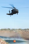 An Arizona Army National Guard UH-60 Black Hawk helicopter from A Company 2-285th Assault Helicopter Battalion stationed in Phoenix slowly climbs into the air after filling a Bambi Bucket with canal water outside Rittenhouse Army Heliport, Queen Creek, Ariz., Dec. 12, 2014. The Guard members conducted wildland firefighting training using the bucket, capable of carrying nearly 530 gallons of water, to pick up and drop water onto target areas.