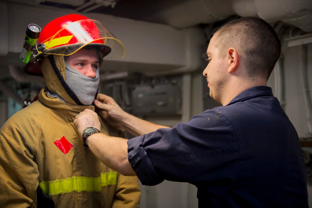 U.S. Navy Petty Officer 2nd Class Jeffrey Taylor, right, assists a sailor donning his firefighting ensemble during a general quarters drill aboard the aircraft carrier USS Carl Vinson in the U.S. 5th Fleet area of operations Jan. 2, 2015. Taylor is a machinist’s mate.