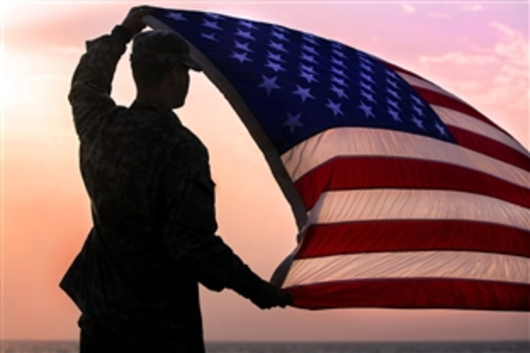 U.S. Army Spc. Morgan Austin holds up the U.S. flag during a promotion and re-enlistment ceremony on  Barclay Training Center, Monrovia, Liberia, Jan. 1, 2015. Austin is a communications specialist assigned to 101st Airborne Division's Headquarters Battalion.