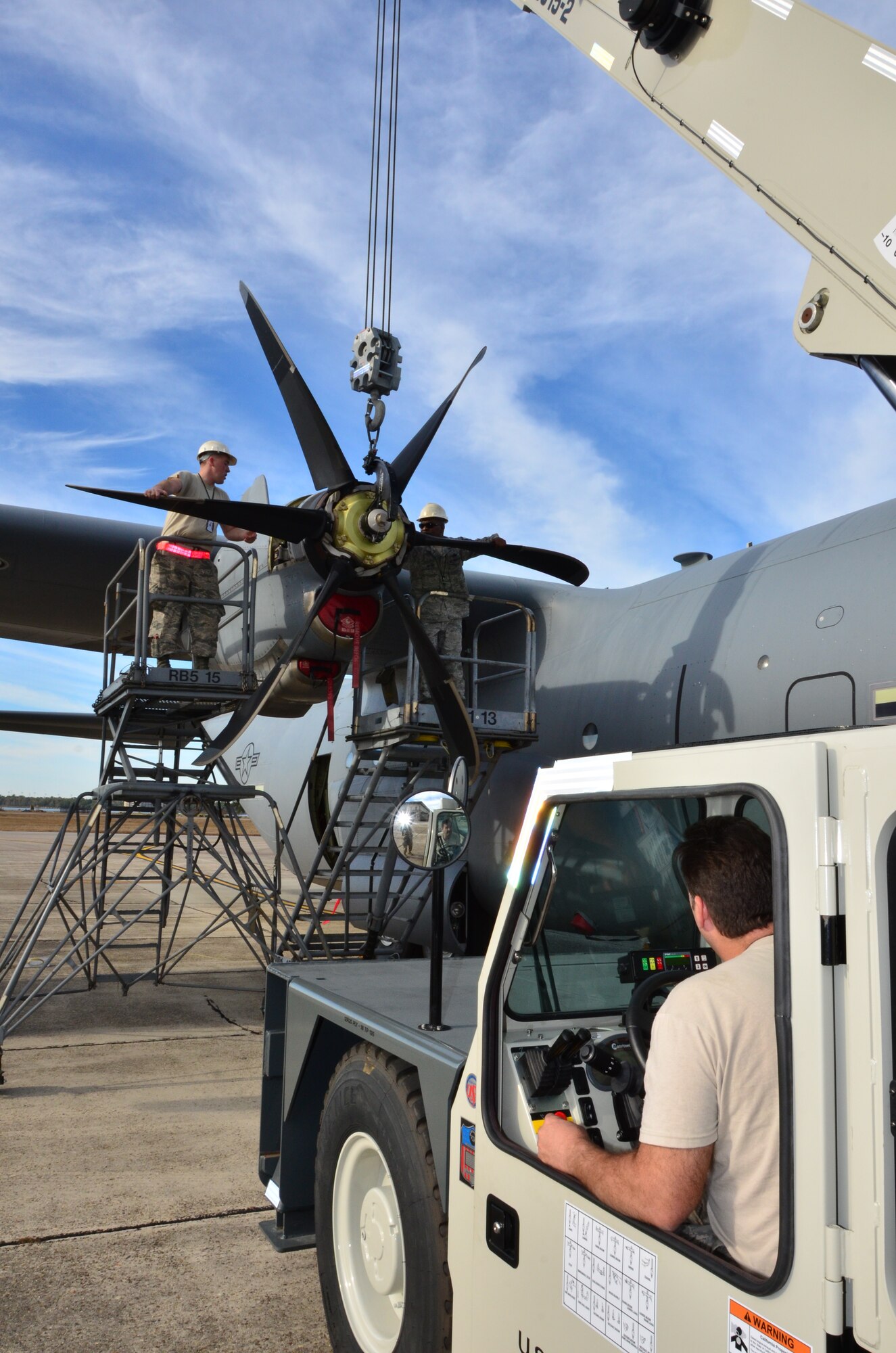 Tech Sgt. Rob Regan slowly guides a crane toward Senior Airman Brandon Reichert and Master Sgt. Donald Maloid, with the 403rd Maintenance Group, while they attempt to reattach a propeller after a repair to a C-130J on the Keesler Air Force Base flightline. (U.S. Photo by/Masters Sgt. Brian Lamar)
