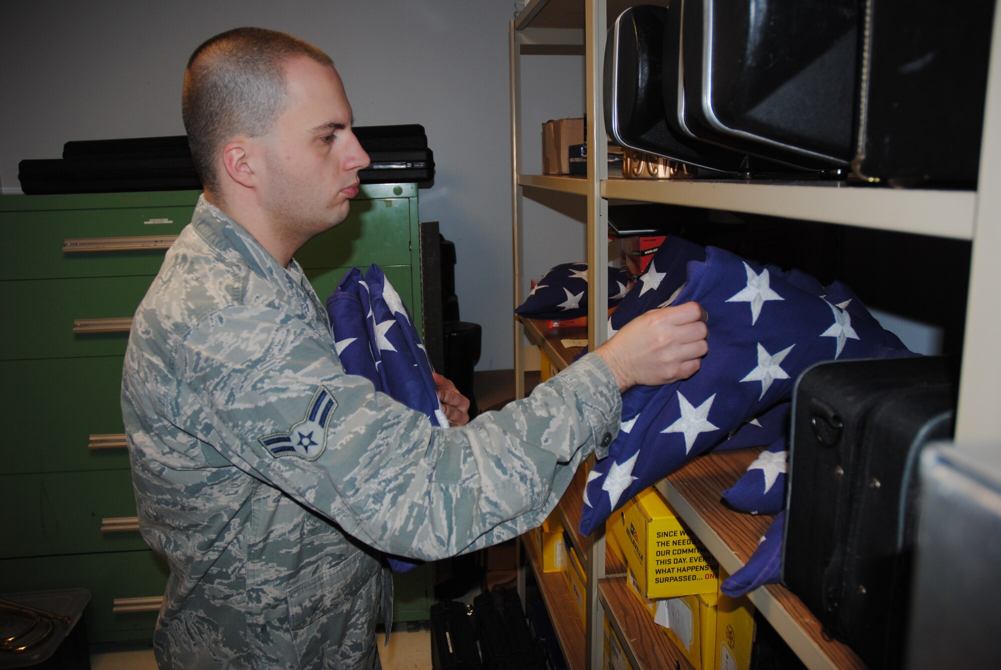 Airman 1st Class Daniel Elmore, a ceremonial guardsman with Grand Forks Air Force Base Honor Guard, organizes a group of U.S. flags onto a shelf inside a storage closet at the Honor Guard Building on Grand Forks AFB, N.D., Dec. 24, 2014. The Base Honor Guard uses several U.S. flags to train and prepare themselves for live ceremonies such as military funerals or a presentation of the colors at public events. , Although the practice flags are used primary for training purposes, the Honor Guard always ensures they never touch the ground or displayed in an undignified manner. (U.S. Air Force photo/Staff Sgt. Luis Loza Gutierrez) 