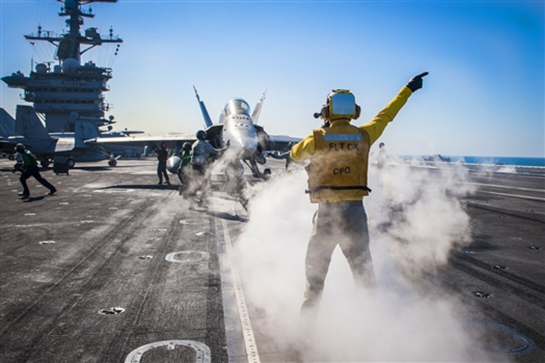 British Navy Chief Callum Gardner directs an F/A-18 Hornet onto a catapult on the flight deck of the aircraft carrier USS Carl Vinson in the Persian Gulf, Jan. 1, 2015.  