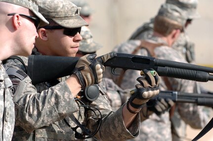 Staff Sgt. Jonathan McDonald (far left), nonlethal weapons instructor for the 49th Military Police Brigade, eyes Sgt. Robert Black of the 217th Military Police Company load a shotgun with nonlethal rounds during range training at Camp Liberty.