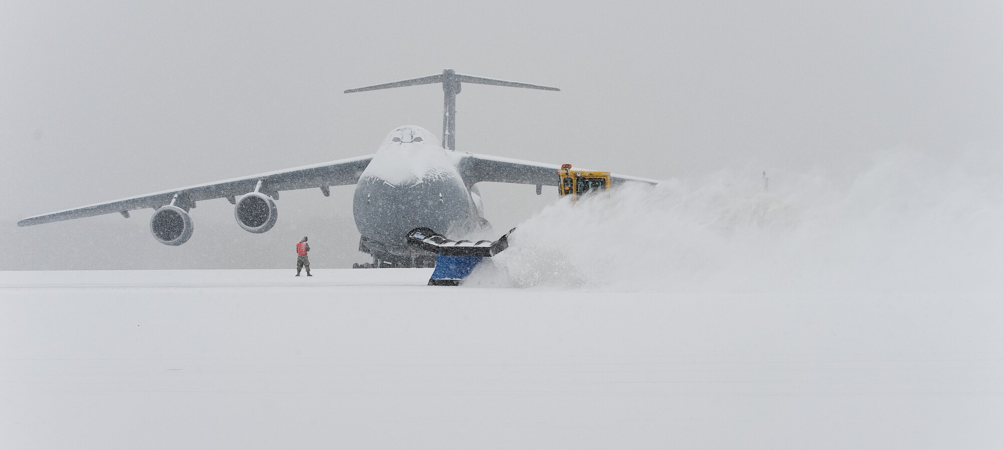 A snow plow from the 436th Civil Engineer Squadron clears snow in front of a snow-covered C-5M Super Galaxy Jan. 6, 2015, at Dover Air Force Base, Del. Snow removal equipment started to clear the flight line, numerous taxiways and two runways around 7:30 a.m. to keep the mission moving. (U.S. Air Force photo/Roland Balik)