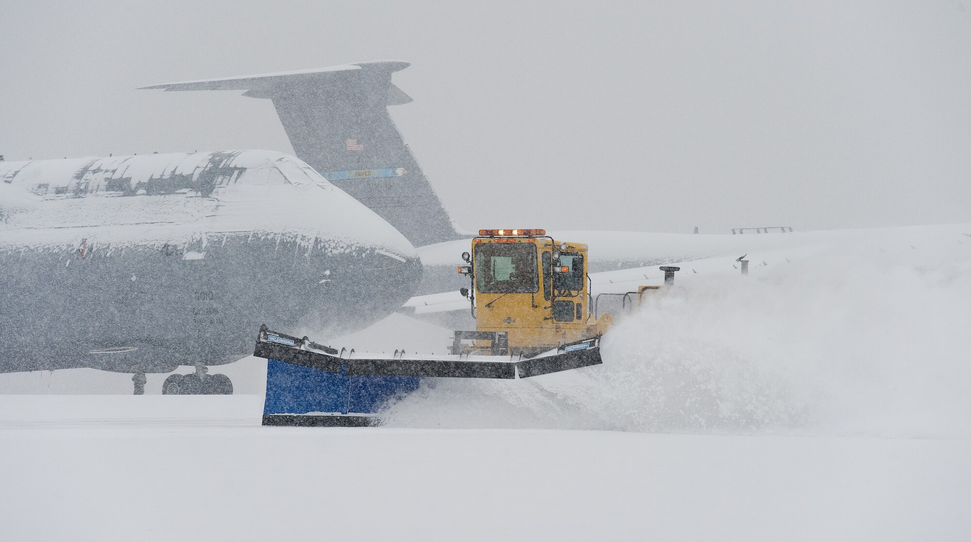 A snow plow from the 436th Civil Engineer Squadron clears snow in front of snow-covered C-5M Super Galaxies Jan. 6, 2015, at Dover Air Force Base, Del. The base continued normal operations as Team Dover personnel initiated snow removal throughout the base. (U.S. Air Force photo/Roland Balik)