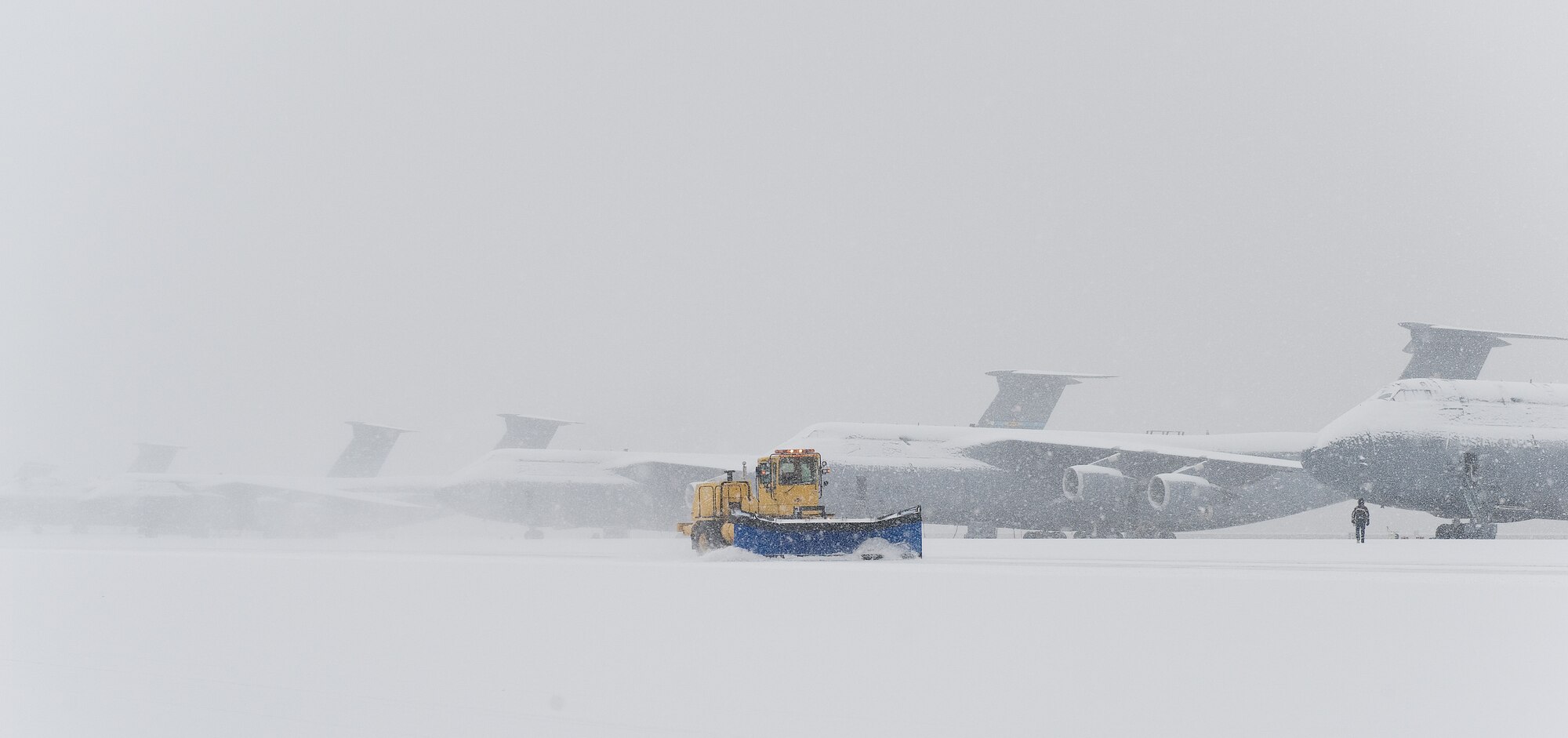 Snow-covered C-5M Super Galaxies sit on the flight line as 436th Civil Engineer Squadron snow removal personnel and equipment plow accumulating snow Jan. 6, 2015, at Dover Air Force Base, Del. The base received 1.4 inches of snow which was the first snowfall of 2015 to blanket the local area. (U.S. Air Force photo/Roland Balik)