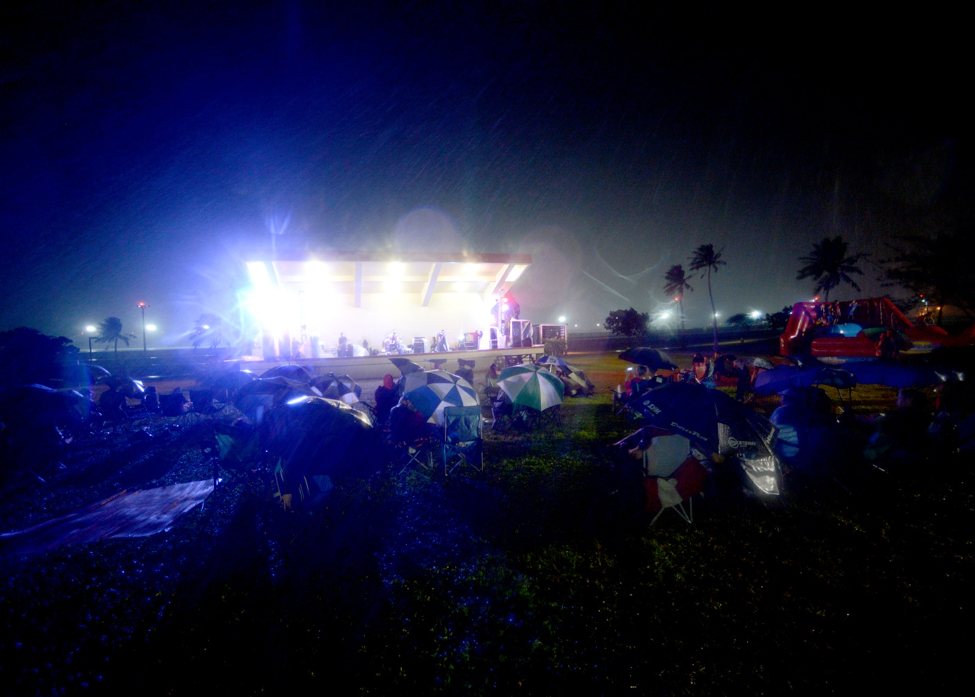 Team Andersen family members hunker down during a rainstorm while alternative rock band Vertical Horizon play on during a free concert Jan. 6, 2015, at the Arc Light Amphitheater at Andersen Air Force Base, Guam. Music fans braved constant rain and wind to hear the band play songs from their double platinum album, Everything You Want. (U.S. Air Force photo by Tech. Sgt. Zachary Wilson/Released.)