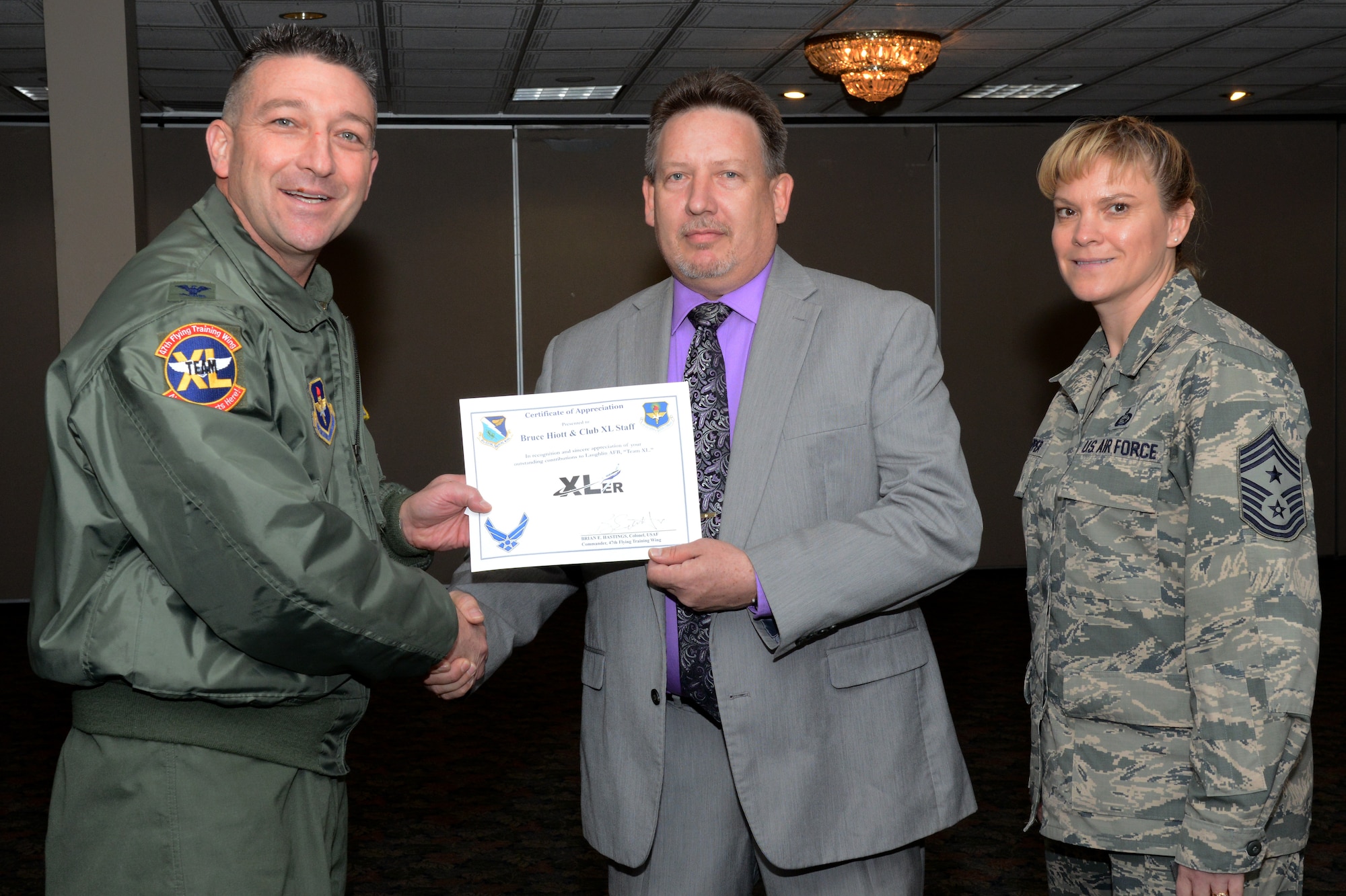 Bruce Hiott, center, Laughlin club operations general manager, poses with Col. Brian Hastings, left, 47th Flying Training Wing commander, and Chief Master Sgt. Teresa Clapper, right, 47th FTW command chief, after accepting the XLer of the week award on behalf of himself and the club staff, here Jan. 7, 2015. The XLer is a weekly award chosen by wing leadership and is presented to those who consistently make outstanding contributions to their unit and Laughlin. (U.S. Air Force photo by Airman 1st Class Ariel D. Delgado)(Released)