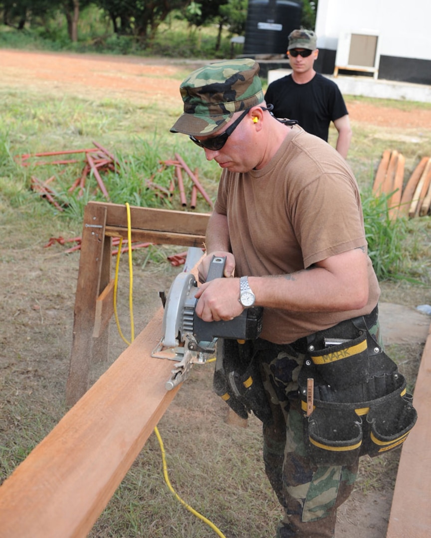 Tech. Sgt. Ken Forche uses a saw to cut a piece of lumber as Senior Airman Derek Leppek holds the board steady during a deployment to Accra, Ghana, April 12, 2010. The 127th Civil Engineering Squadron of the Michigan Air National Guard deployed to Ghana for two weeks to help perform a major renovation on this training building used by the air force of Ghana.