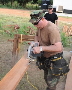 Tech. Sgt. Ken Forche uses a saw to cut a piece of lumber as Senior Airman Derek Leppek holds the board steady during a deployment to Accra, Ghana, April 12, 2010. The 127th Civil Engineering Squadron of the Michigan Air National Guard deployed to Ghana for two weeks to help perform a major renovation on this training building used by the air force of Ghana.