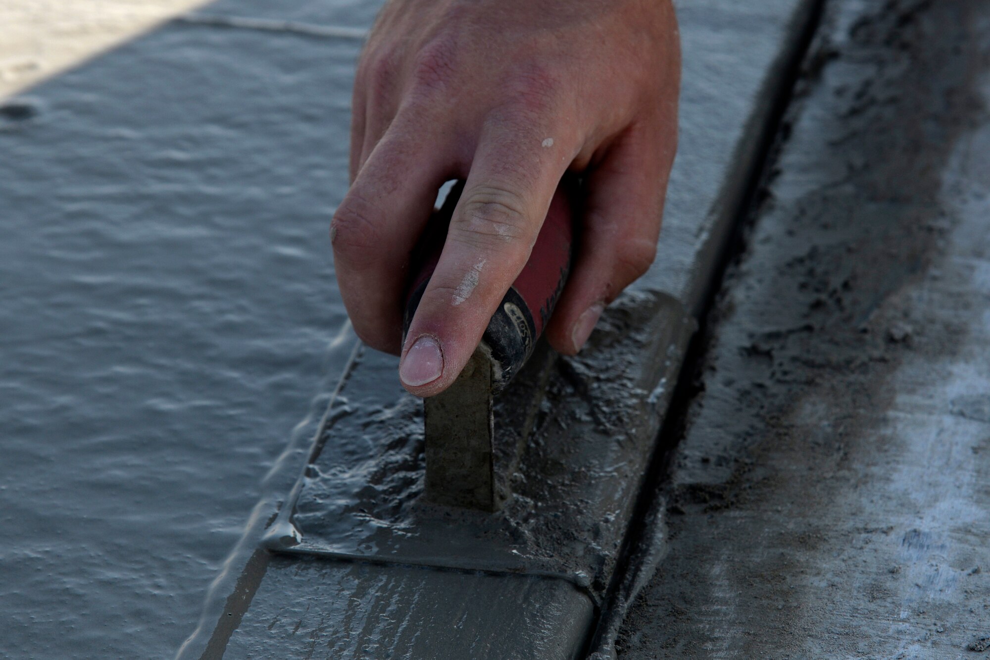 An Airman with the Expeditionary Civil Engineer Squadron smoothes the edges of fresh laid concrete at the Australian beddown site on an undisclosed location in Southwest Asia Oct. 30, 2014. Airmen with the ECES worked side-by-side with their Australian counterparts as they collectively constructed a beddown site from the ground up. (U.S. Air Force photo/Tech. Sgt. Marie Brown)