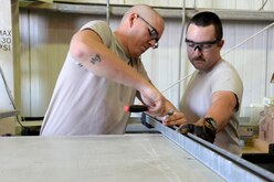 Staff Sgts. Kiah, left, and Kyle, Expeditionary Civil Engineer Squadron, structural craftsmen, put the finishing touches on the main power distribution panel set to be installed at the Australian beddown site at an undisclosed location in Southwest Asia, Oct. 28, 2014. The structures shop's responsibilities include roof repairs, replacing doors and glass, metal working, masonry and carpentry. Kiah is deployed out of Grand Forks Air Force Base, N.D. and Kyle is deployed out of Mountain Home Air Force Base, Idaho. (U.S. Air Force photo by Tech. Sgt. Marie Brown)