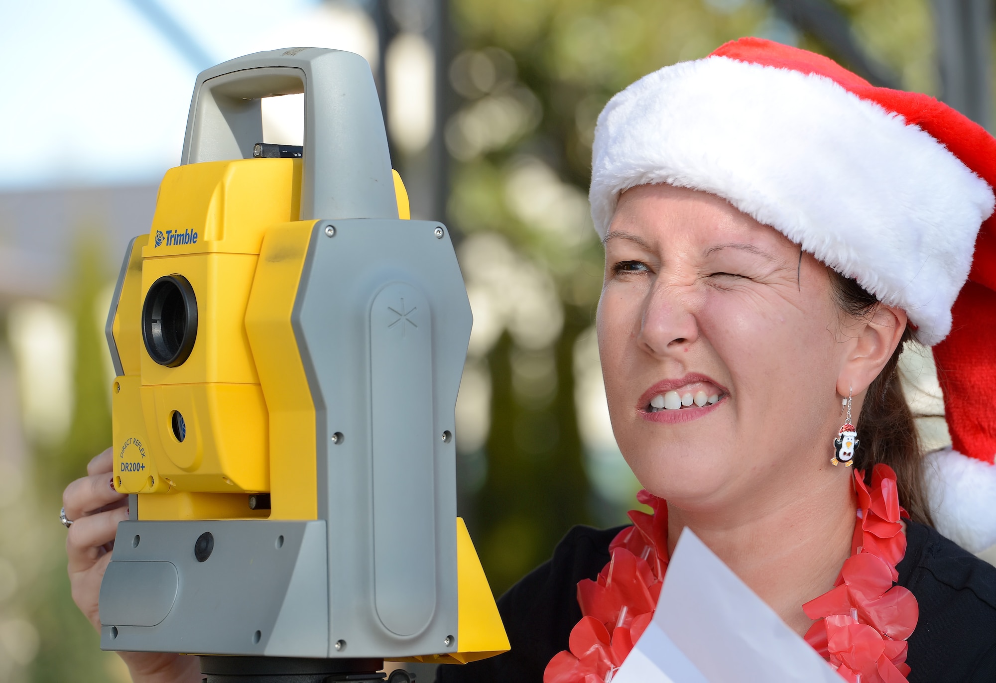Laura Tasker, wife of Lt. Col. Donald Tasker, 436th Force Support Squadron commander, closes one eye while moving her head toward the eyepiece of a Trimble DR200+ Geodimeter surveying station while participating in the 2014 Dover Officers' Spouses' Club Amazing Race competition Dec. 18, 2014, at Dover Air Force Base, Del. Teams had to look through the surveying equipment to find small numbers posted on an object far away which gave them the building number for their next clue. Tasker  was part of the 'Santa Babes' Amazing Race team. (U.S. Air Force photo/Greg L. Davis)