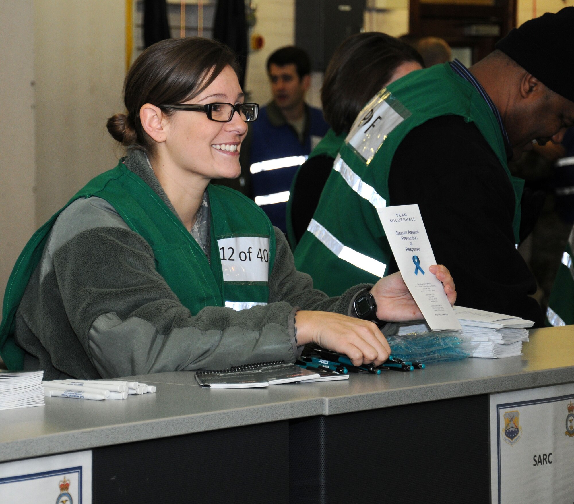 U.S. Air Force Tech. Sgt. Vanessa Kroening, 352nd Special Operations Maintenance Squadron NCO in charge of maintenance instruction from O'Fallon, Ill., hands out flyers to Team Mildenhall members as they go through a personnel deployment function line during an operational readiness exercise Jan. 7, 2015, on RAF Mildenhall, England. During this part of the exercise, Kroening is a sexual assault prevention and response victim advocate offering advice and information. (U.S. Air Force photo by Gina Randall/Released)