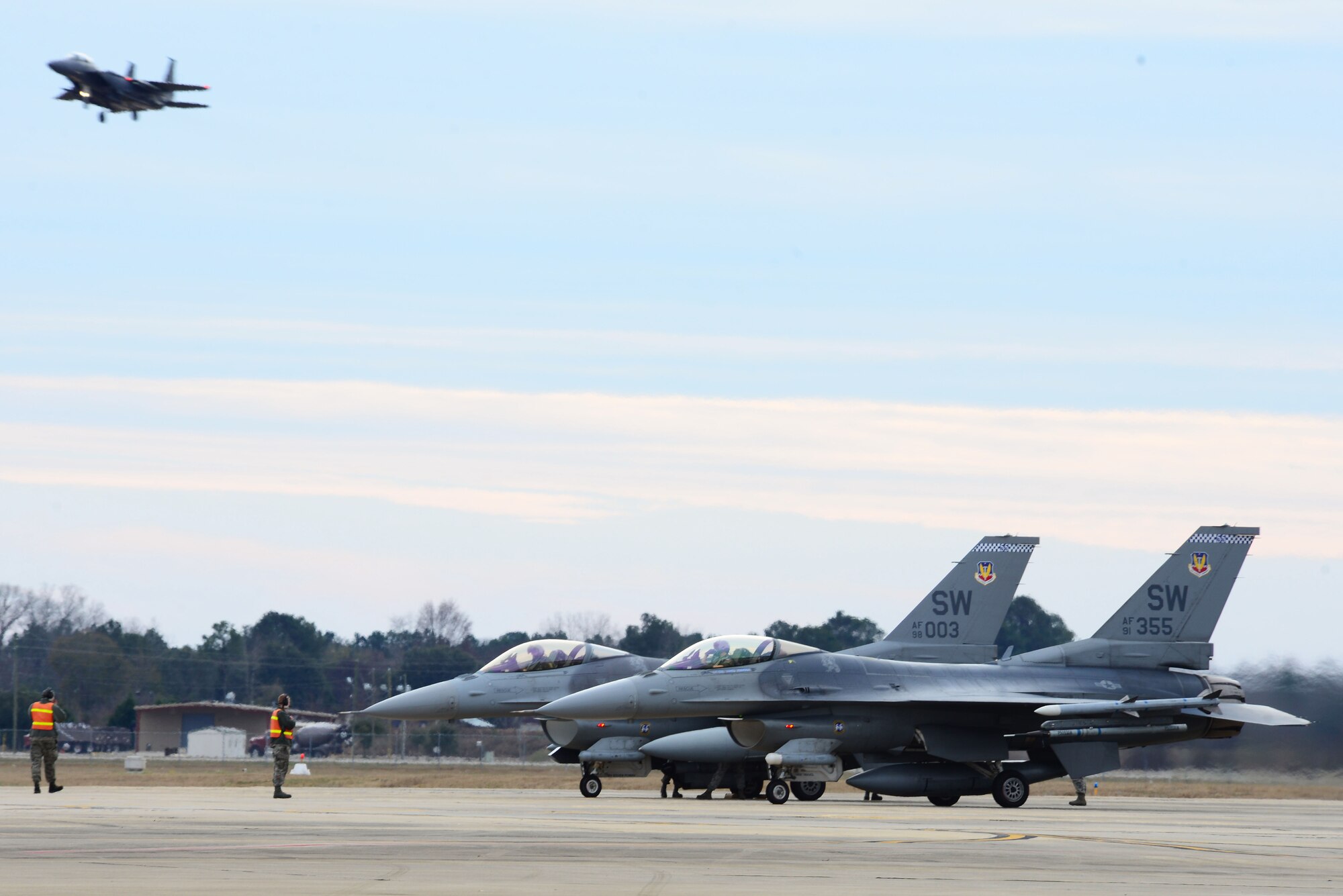 U.S. Air Force F-16CM Fighting Falcons perpare to take off as an F-15 Strike Eagle assigned to Seymore Johnson Air Force Base, N.C. flys by, at Shaw Air Force Base, S.C., Jan. 7, 2015. The F-16 is a compact, multi-role, highly maneuverable fighter aircraft. (U.S. Air Force photo by Airman 1st Class Michael Cossaboom/Released)