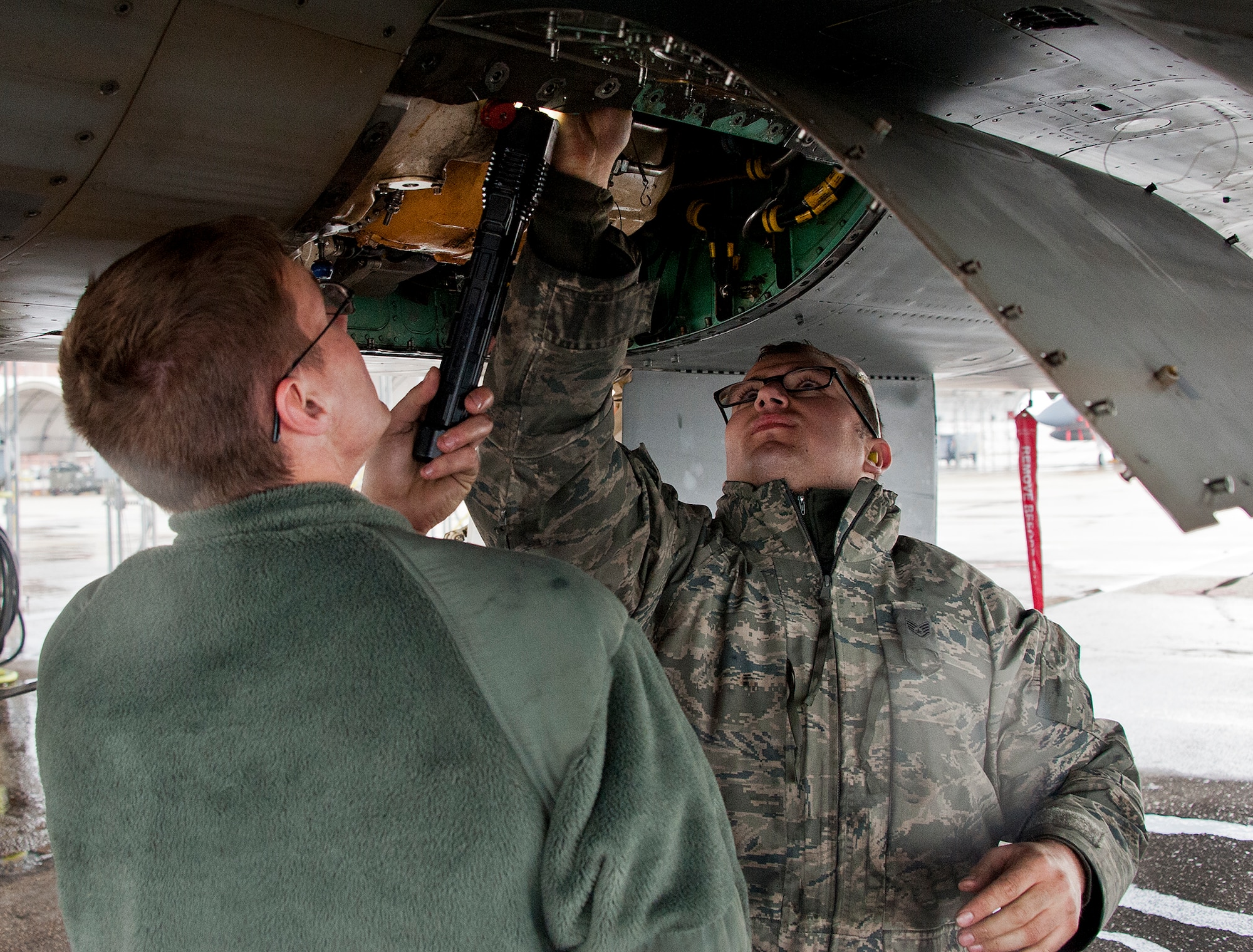 Senior Airman James Griggs, of the 96th Aircraft Maintenance Squadron, holds a flashlight while Senior Airman Carl Sutherland, also of the 96th AMXS, examines a pump in the under carriage of an F-15 Eagle at Eglin Air Force Base, Fla. on Dec. 19.  The crew chiefs verified the proper installation of a new pump shaft seal after a hydraulic leak was identified.  All the test aircraft for the 96th Test Wing and the 85th Test and Evaluation Squadron are maintained by the 96th AMXS. (U.S. Air Force photo/Ilka Cole)