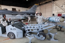 Senior Airman Gavin Moses (left), 80th Aircraft Maintenance Unit weapons load crew member, and Staff Sgt. Trumaine Cox, 80th AMU weapons load crew chief, raise their hands as they prepare to load a GBU-38 bomb on a BRU-57 bomb rack during the fourth quarter weapons loading competition Jan. 9, 2015, at Kunsan Air Base, Republic of Korea.  With just an 11-point lead, Cox, Wilsey, and Senior Airman Gavin Moses of crew 40 from the 80th AMU were named the winners. (U.S. Air Force photo by Senior Airman Katrina Heikkinen/Released)
