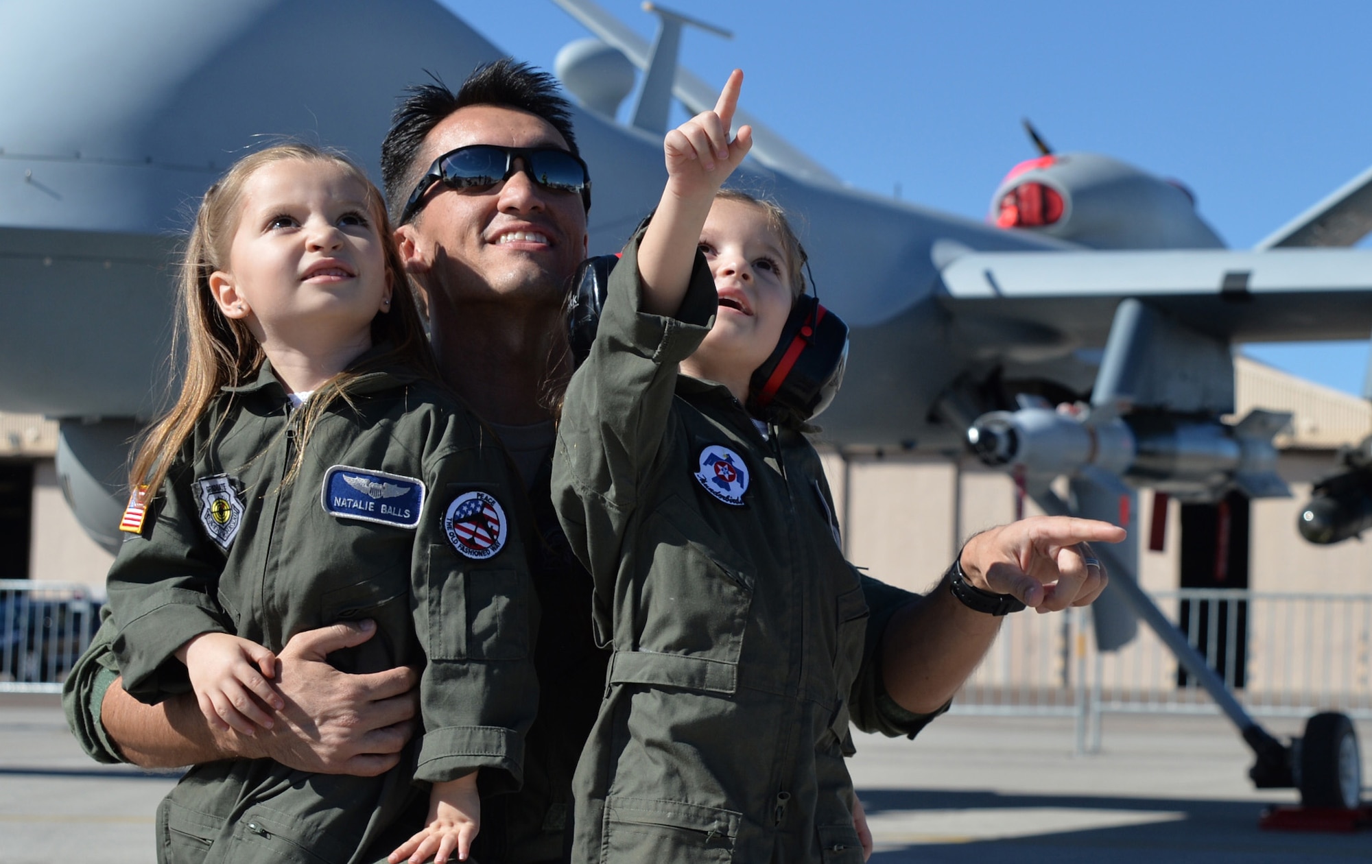 Natalie and Melanie watch the Legacy Bombers fly with their father Capt. Eric for the friends and family day at the 2014 Open House on Nellis Air Force Base, Nev., Nov. 7, 2014. The Open House is a two-day event that will depict the history of American aviation and salute recent accomplishments of America's military in operations around the globe through numerous military and civilian ground displays. (U.S. Air Force photo by Tech. Sgt. Nadine Barclay/Released) (Names withheld for security)