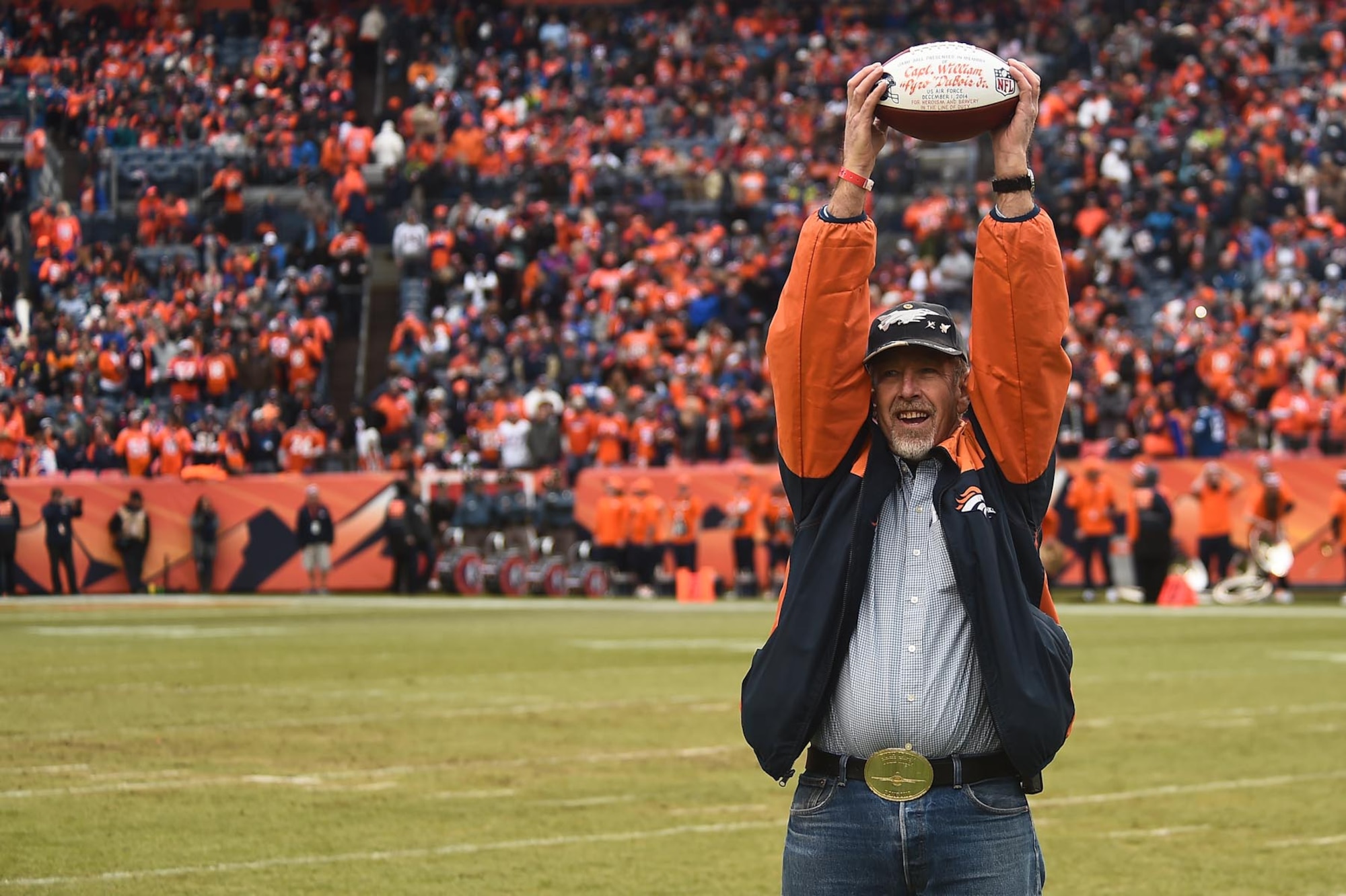 William “Ham” DuBois, the father of Capt. William H. DuBois, raises the game ball in front of thousands of cheering fans Jan. 11, 2015, at Sports Authority Field in Denver. The family of the fallen pilot, Capt. DuBois, was presented the game ball before the Denver Broncos playoff game to honor his service and sacrifice. (U.S. Air Force photo by Airman 1st Class Luke W. Nowakowski/Released) 