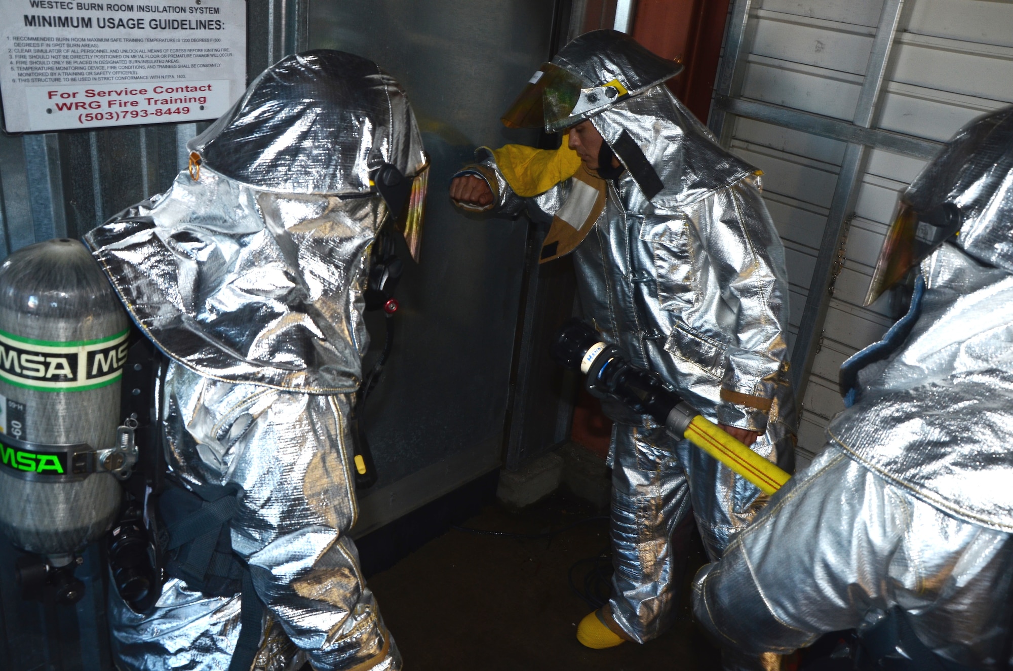 Tech. Sgt. Kaweo Andreas-Feeney, center, a safety officer with the 624th Civil Engineering Squadron, uses his hand to test the heat of the door before two firefighters, far left and right, also with the 624th CES, enter the room where a kitchen fire has been simulated with propane gas, Hickam Field, Hawai'i, Jan. 10, 2015. (U.S. Air Force photo by Tech. Sgt. Phyllis Keith)
