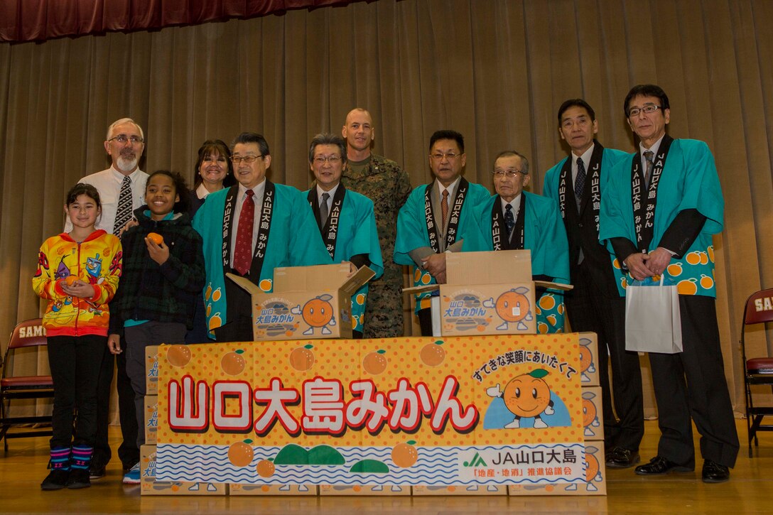 Members of the local Iwakuni agricultural and societal cooperative associations pose for a photo with Lt. Col. Mike Carreiro, executive officer of Marine Corps Air Station Iwakuni, Japan, and members of the Matthew C. Perry Elementary School’s faculty and student body during the school’s mikan presentation inside the school’s gymnasium, Jan. 13, 2015, aboard station. The purpose of the event was to strengthen the bond between Iwakuni City residents and M.C. Perry students. Members of the associations presented M.C. Perry Elementary School with 20 boxes of mikans from Suo-Oshima Island.