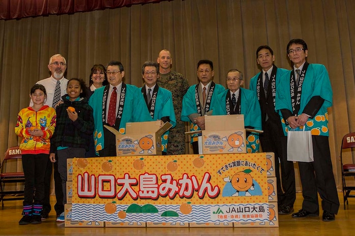 Members of the local Iwakuni agricultural and societal cooperative associations pose for a photo with Lt. Col. Mike Carreiro, executive officer of Marine Corps Air Station Iwakuni, Japan, and members of the Matthew C. Perry Elementary School’s faculty and student body during the school’s mikan presentation inside the school’s gymnasium, Jan. 13, 2015, aboard station. The purpose of the event was to strengthen the bond between Iwakuni City residents and M.C. Perry students. Members of the associations presented M.C. Perry Elementary School with 20 boxes of mikans from Suo-Oshima Island.