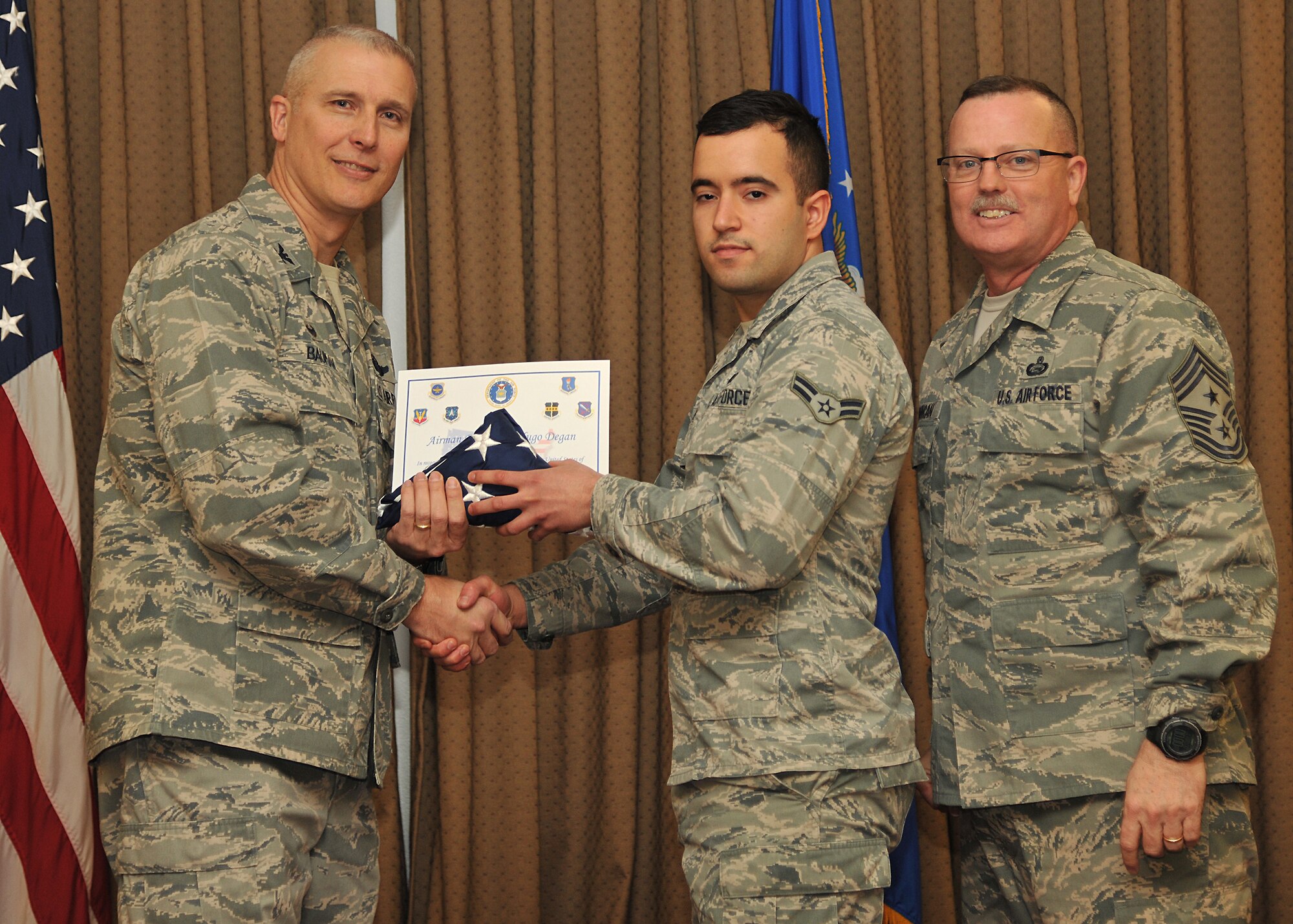 Col. Paul Bauman, 319th Air Base Wing commander, and 319th ABW Command Chief Master Sgt. David Duncan, pose for a photo with Airman 1st Class Hugo Degan after presenting him with a U.S. flag  and certificate of recognition during a wing quarterly awards ceremony held Jan. 15, 2015, at the Northern Lights Club on Grand Forks Air Force Base, N.D. The Airman from the 319th Force Support Squadron was one of six Warriors of the North recognized by the base for becoming naturalized U.S. citizens in 2014. (U.S. Air Force photo/Senior Airman Xavier Navarro)