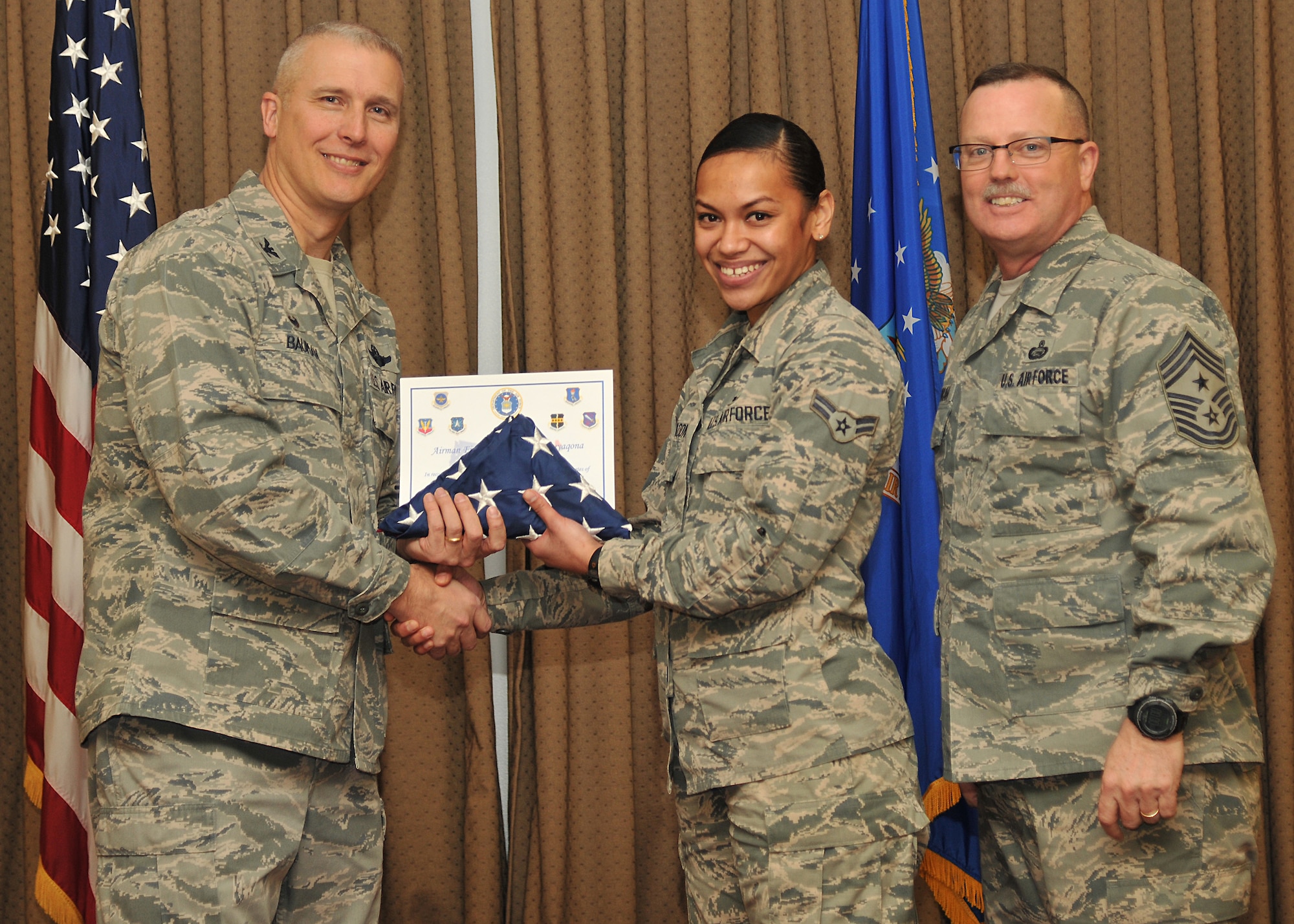 Col. Paul Bauman, 319th Air Base Wing commander, and 319th ABW Command Chief Master Sgt. David Duncan, pose for a photo with Airman 1st Class Irinieta Tabuyaqona after presenting her with a U.S. flag and certificate of recognition during a wing quarterly awards ceremony held Jan. 15, 2015, at the Northern Lights Club on Grand Forks Air Force Base, N.D. The Airman from the 319th Contracting Flight was one of six Warriors of the North recognized by the base for becoming naturalized U.S. citizens in 2014. (U.S. Air Force photo/Senior Airman Xavier Navarro)