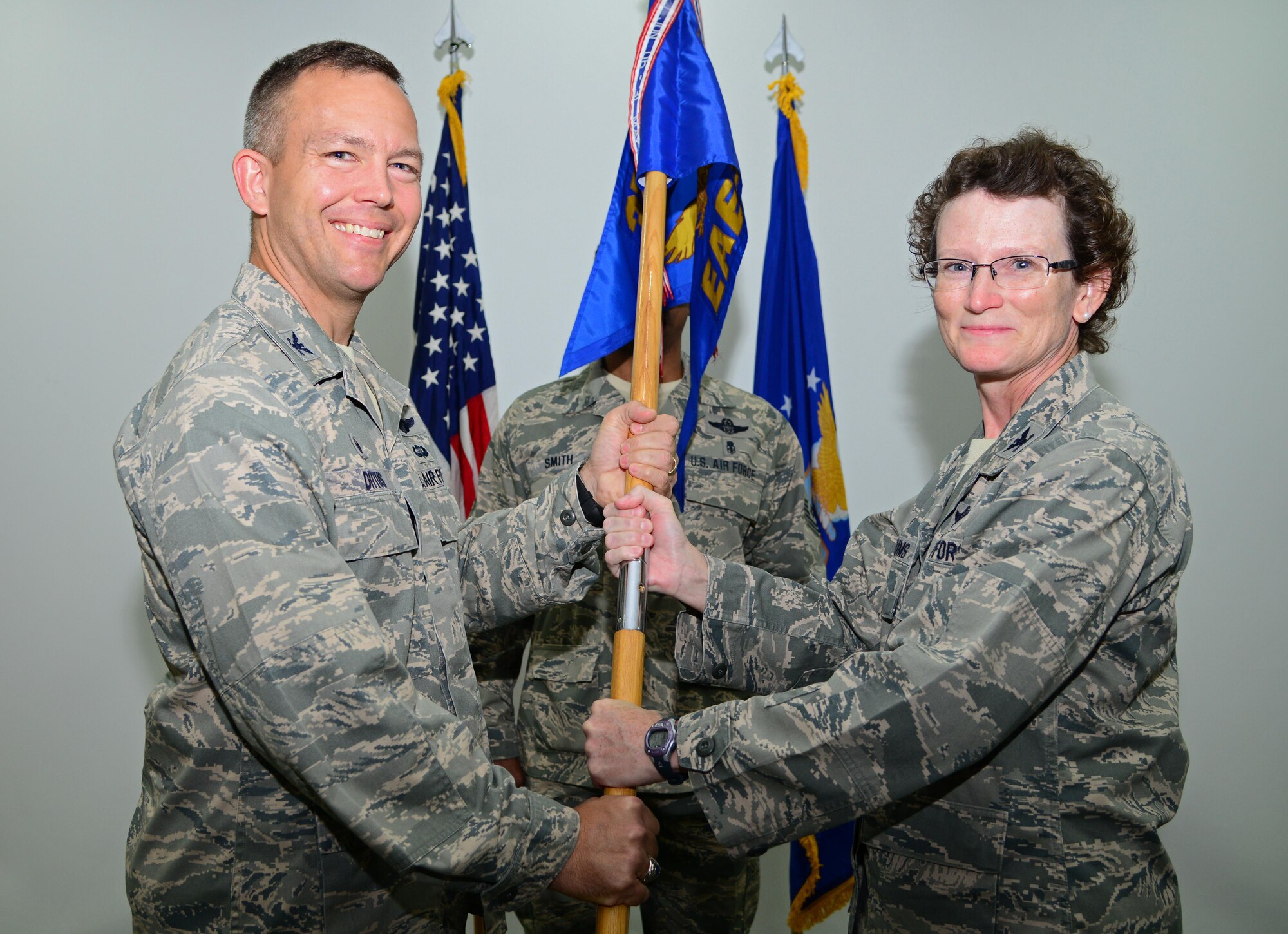 U.S. Air Force Col. Janet Sessums, right, passes the 379th Expeditionary Aeromedical Evacuation Squadron guidon to Col. Jim Dittus, 379th Expeditionary Operations Group commander, to  officially relinquish command during a change of command ceremony, Jan. 14, 2015, at Al Udeid Air Base, Qatar. Sessums relinquished command of the 379th EAES to Lt. Col. June Oldman. (U.S. Air Force photo by Senior Airman Kia Atkins)