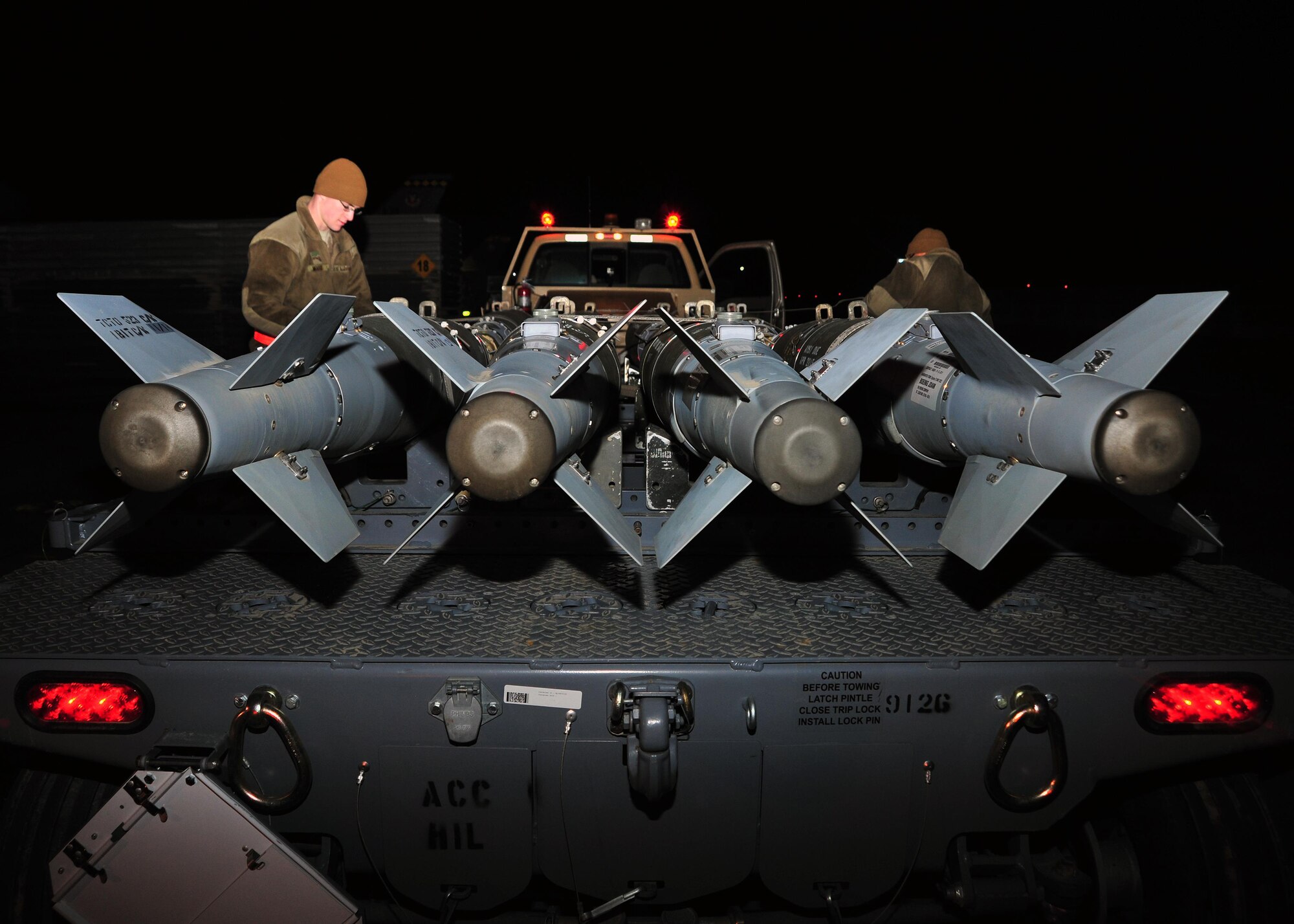 U.S. Air Force Airman 1st Class Vincent Martinez and U.S. Air Force Airman 1st Class Jared Moore, 455th Expeditionary Maintenance Squadron line delivery crew members, loosen the straps on a transportation trailer in preparation for a munitions load Jan. 14, 2015 at Bagram Airfield, Afghanistan. Line delivery Airmen have completed 741 munitions deliveries since October, ensuring the timely facilitation of airpower to the U.S. Central Command area of responsibility. (U.S. Air Force photo by Staff Sgt. Whitney Amstutz/released)
