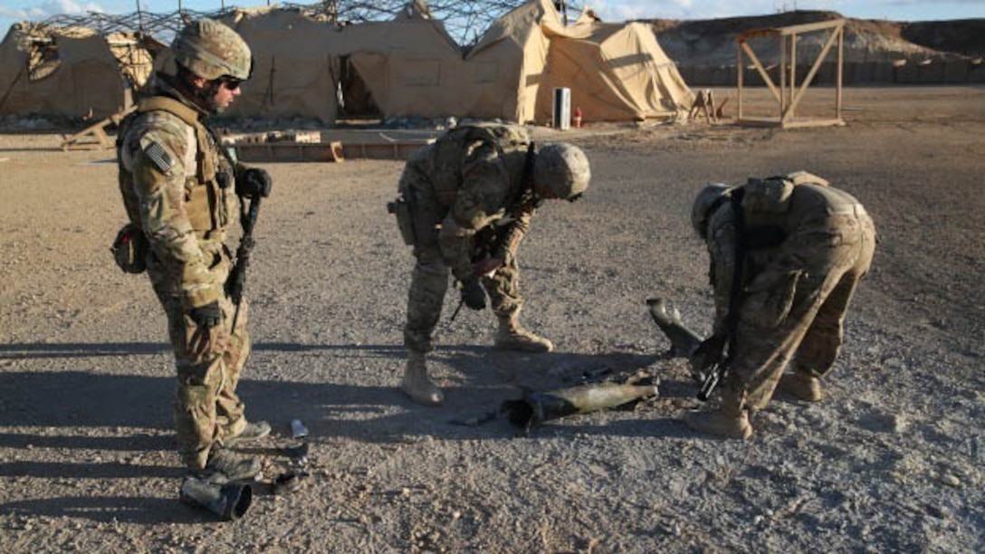 Cpl. Mike Smith (left), Staff Sgt. Steve Fitzpatrick (center), and Spc. Kevin Braun (right), members of a U.S. Army Explosive Ordnance Disposal Company, Task Force Al Asad, examine the point of impact of a 122 mm rocket aboard Al Asad Airbase, Iraq, Jan. 4, 2015. Soldiers and Marines are taking prudent measures to protect the members of Task Force Al Asad from the threat of indirect fire. 