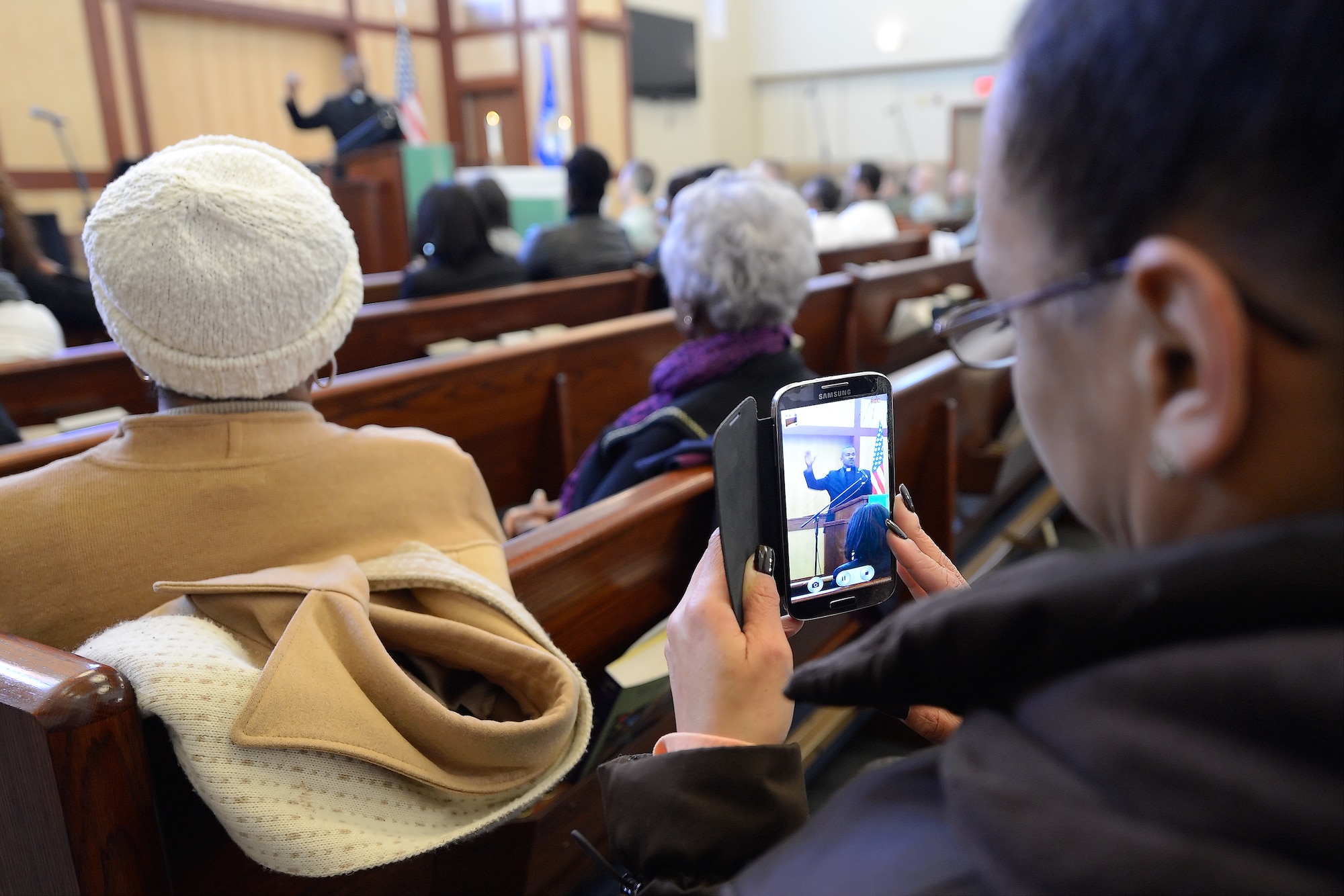 Maria McElroy, Air Force Mortuary Affairs Operations, Program and Facilities branch chief, uses her smart-phone to record Rev. Dr. John Moore Sr., recounting Dr. Martin Luther King Jr.'s, 'I have a Dream Speech,' on Jan. 15, 2015, at the Dover Air Force Base, Del., main chapel. Moore was the guest speaker for the Dr. Martin Luther King Jr. Day Commemoration Service hosted by the 436th Airlift Wing.  (U.S. Air Force photo/Greg L. Davis)