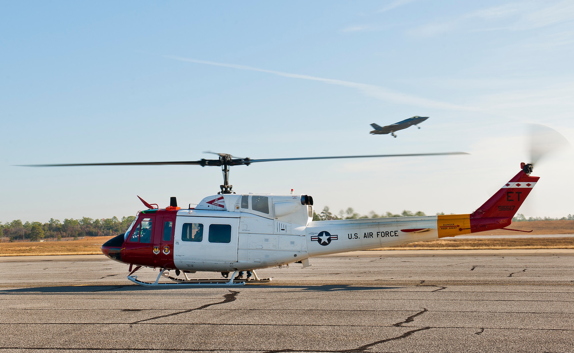 A 413th Flight Test Squadron UH-1 Huey spins up as an F-35 Lightning II completes a low-level pass to the runway at Duke Field, Fla.  The 413th FLTS provides developmental testing to rotary wing aircraft such as the UH-1, CV-22 and the C-130.  (U.S. Air Force photo/Samuel King Jr.)