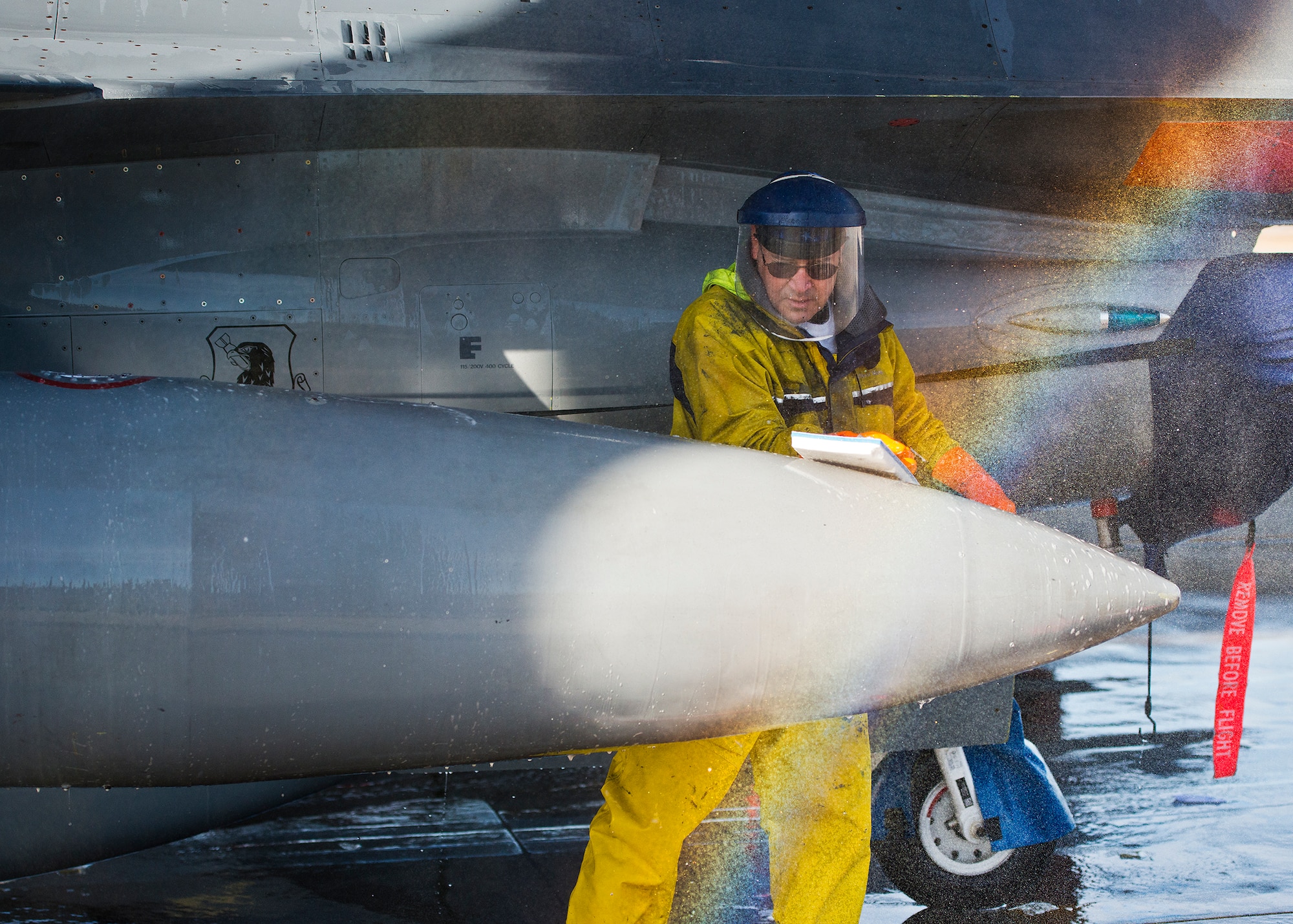Spray from the water hose creates a misty rainbow in front of Jose Vega, a contractor with PAE, as he wipes down the external fuel cell of an F-16 Fighting Falcon at Eglin Air Force Base, Fla. PAE maintains the 96th Test Wing wash rack and also supports armament, engines, sheet metal, aero repair, metals tech, non-destructive inspection, aircraft phase dock and fuels repair shop. (U.S. Air Force photo/Samuel King Jr.)