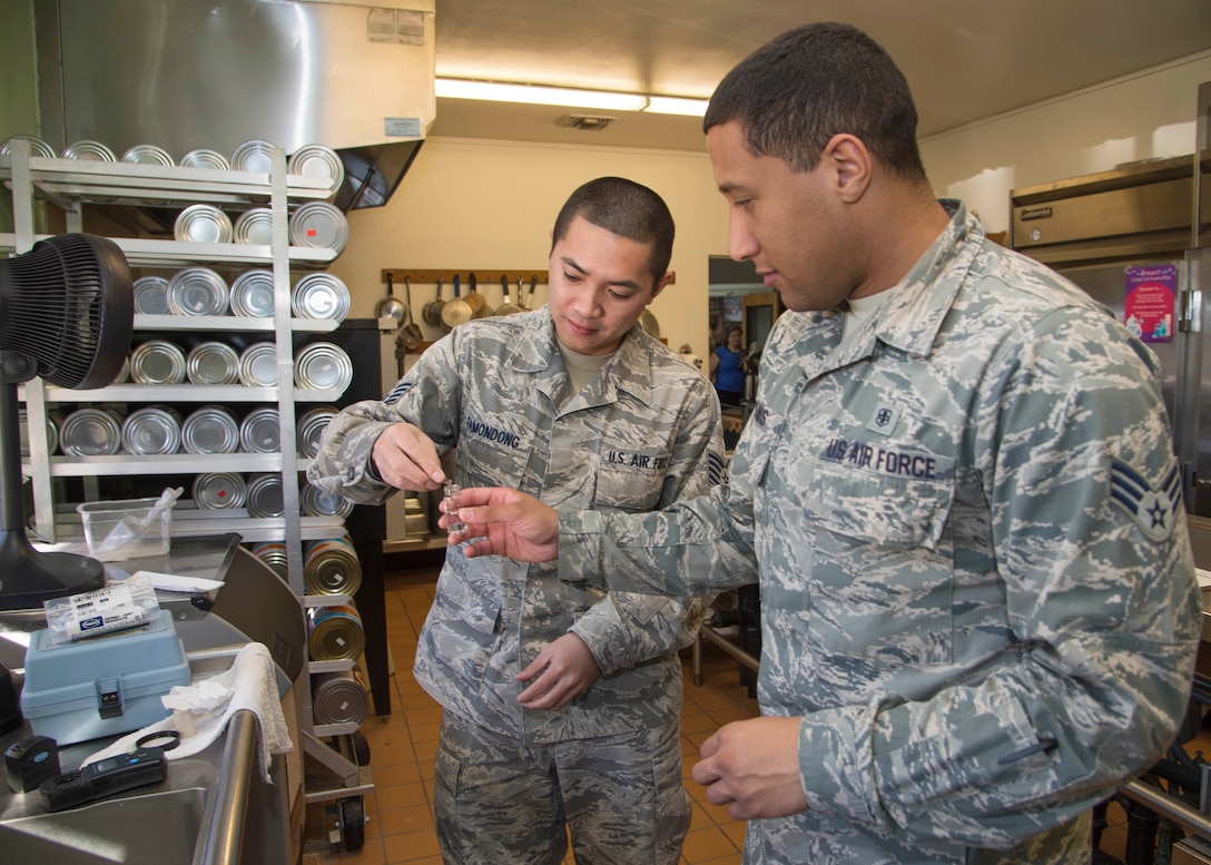 Staff Sgt. Harold King Pascual Tamondong and Senior Airman Andrew Travis add a reagent to a drinking water sample collected at the Child Development Center Youth Annex kitchen. The results will identify the level of chlorine present. Chlorine levels indicate how well the drinking water system disinfection process is operating. (U.S. Air Force photo by Ethan Wagner)