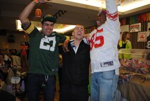 (On opposite ends) Senior Airmen Michael Dalton and John Shaw enthusiastically celebrate 2nd Lt. Christopher Elworth winning the Super Base Extravaganza bingo grand prize of a trip to Super Bowl XLIX Jan. 17, 2015, at the Northern Lights Club t Grand Forks Air Force Base, N.D. The trip to the Super Bowl in Arizona was retail valued at more than $13,000. (U.S. Air Force photo/Staff Sgt. Luis Loza Gutierrez)