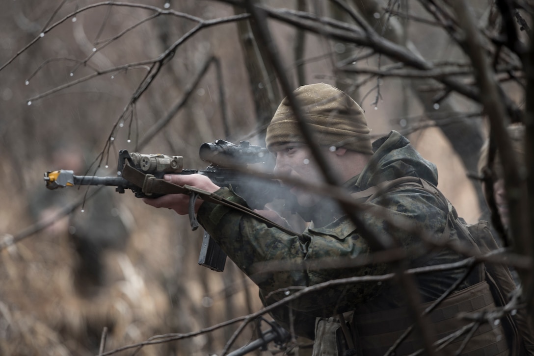A Sailor with the 1st Batallion, 1st Marines, simulates weapon fire shooting blanks toward escaping aircrew members during joint training Jan. 16, 2015 at Camp Fuji, Japan. The Marines, who were acting as enemy aggressors searching for Air Force aircrew during survival, evasion, resistance and escape training, also practiced their small arms engagement with a “rescue” team of Marines. (U.S. Air Force photo/Staff Sgt. Cody H. Ramirez/)