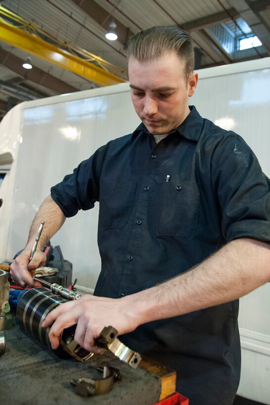 Senior Airman Joseph Hooker, 51st Logistics Readiness Squadron general purpose mechanic, compresses the rings on a piston at Osan Air Base, Republic of Korea, Dec. 22, 2014. The compression of the piston rings is done in order to place the piston back into the engine block. (U.S. Air Force photo by Senior Airman Matthew Lancaster)