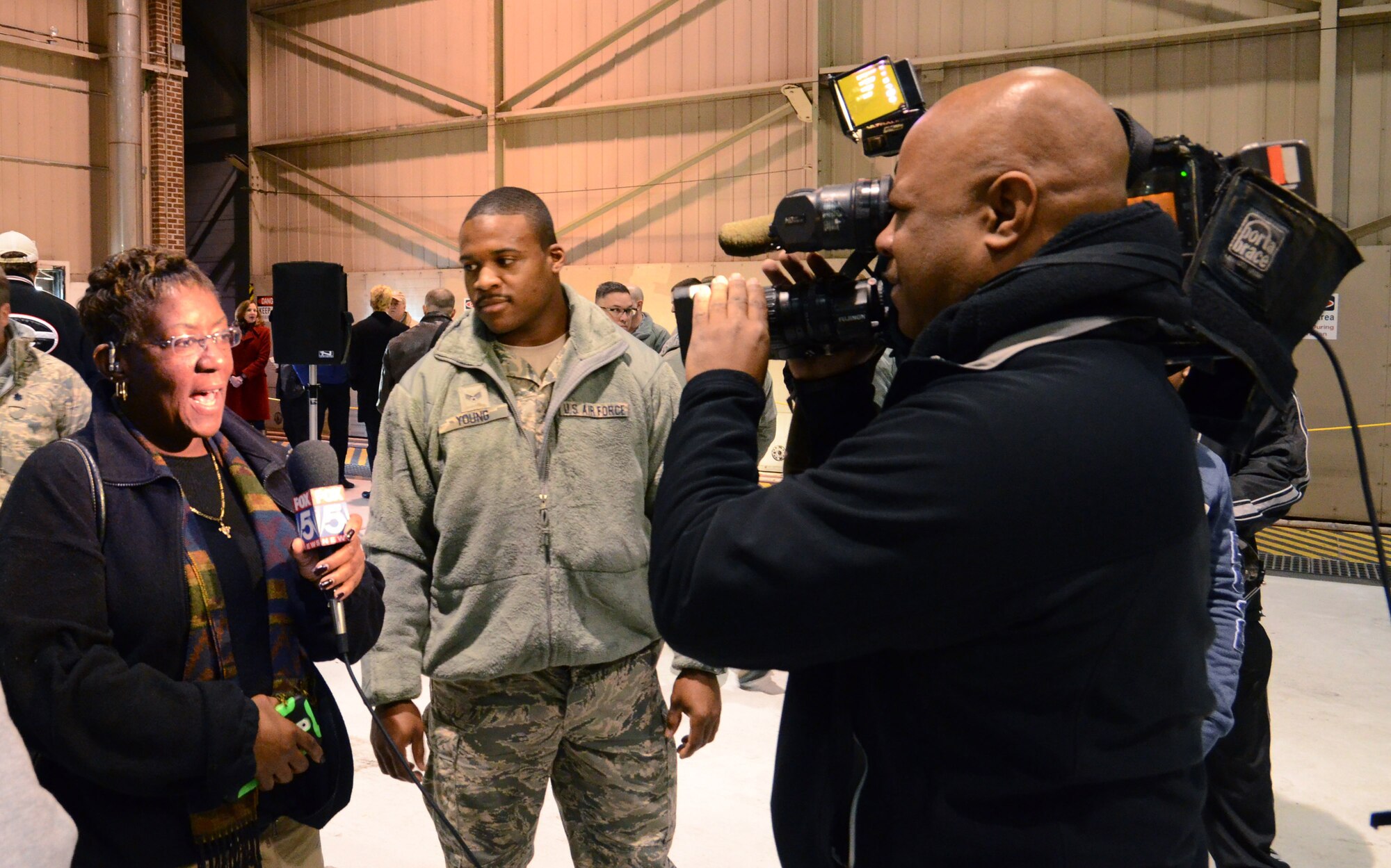 Senior Airman Malcolm Young looks on as his mother is interviewed by Fox 5 news at the deployment send-off, Jan. 8, 2015 at Dobbins Air Reserve Base, Ga.  (U.S. Air Force photo/Brad Fallin)