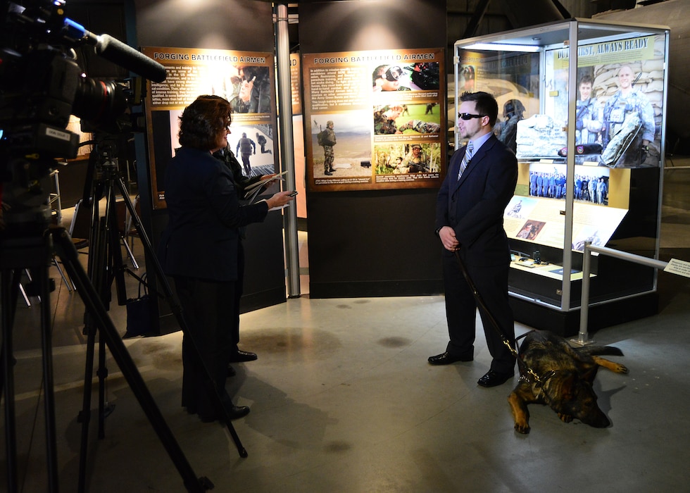 A veteran stands in front of an exhibit conducting an interview.