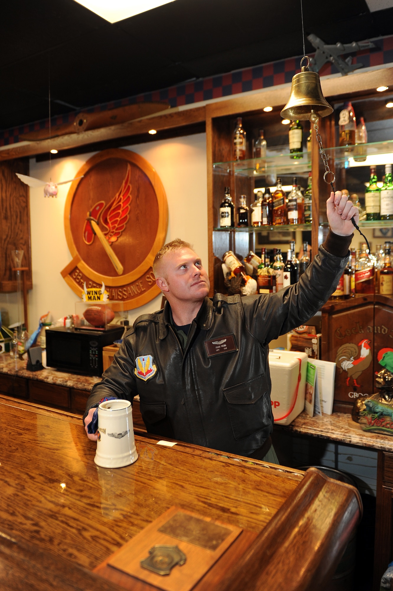 U.S. Air Force Capt. Adam Weink, 38th Reconnaissance Squadron’s heritage room mayor, rings the bell located above the bar following the weekly roll call on Jan. 9, Offutt Air Force Base, Neb.  The bell is rung for a variety of reasons and is fixture in many heritage rooms.  (U.S. Air Force photo by Josh Plueger/Released)