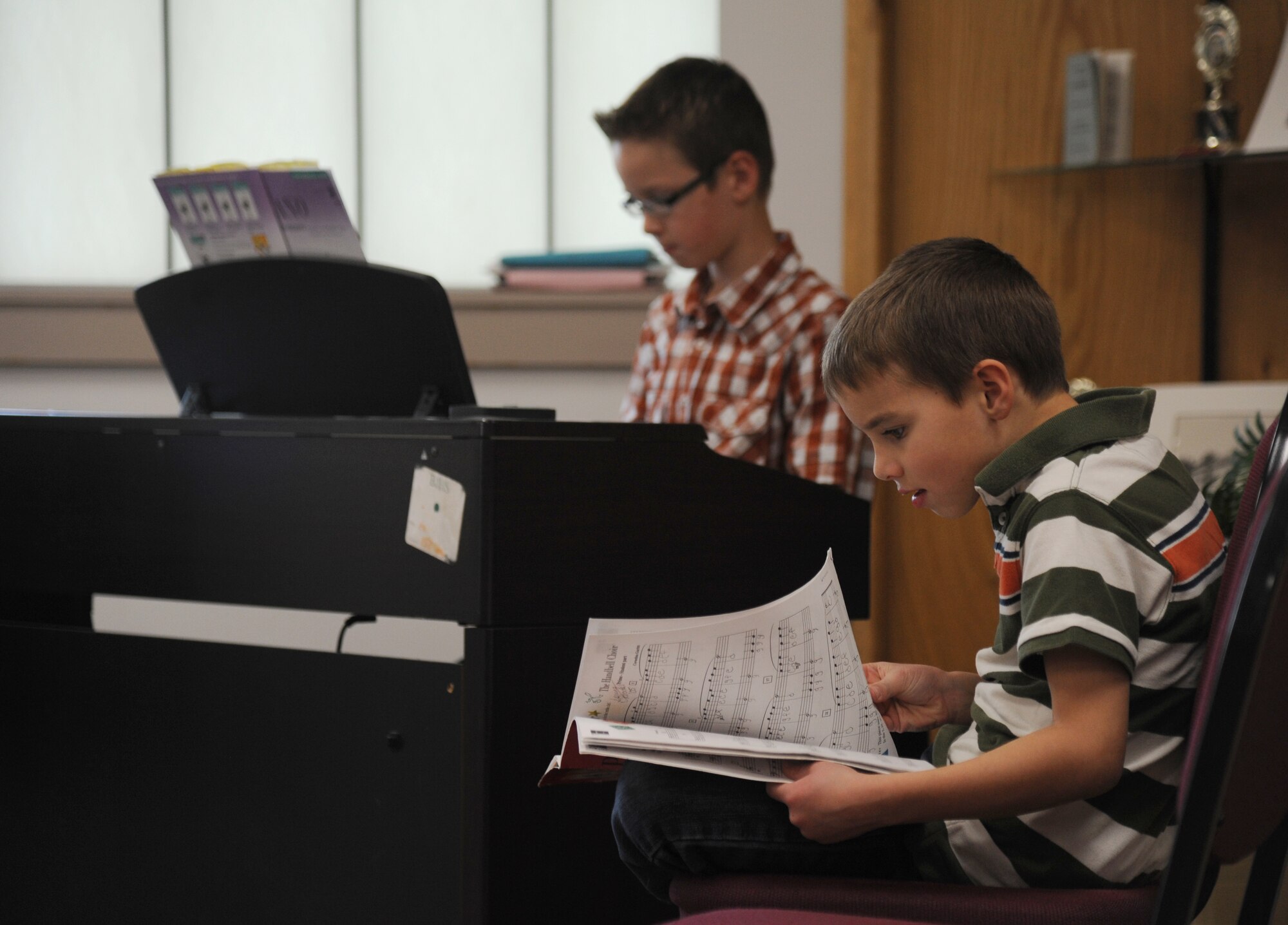 The sons of Maj. Jeremiah Parker, 81st Dental Squadron resident, plays piano while his brother reads over music sheet during a Biloxi Public School Board meeting Jan. 20, 2015, at the Dukate Building, Biloxi, Miss. The meeting was hosted by Jeff Davis Elementary School who selected talented children to perform for the board, which meets monthly. (U.S. Air Force photo by Kemberly Groue)