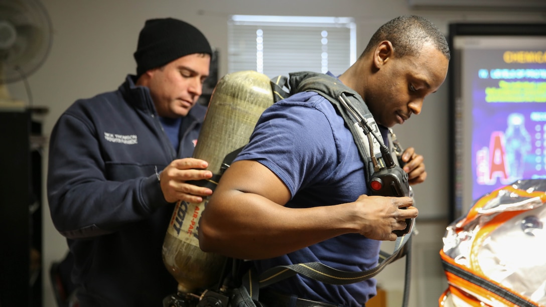Nick Thomson, base firefighter and paramedica, helps Layne Jackson, base firefighter and emergency medical technician, into his gear to show students hazardous waste protective gear during the Hazardous Waste Operations and Emergency Response course aboard Marine Corps Air Station Beaufort, Jan. 14. HAZWOPER training is vital for safety aboard the Air Station, which has many hazardous waste risks.