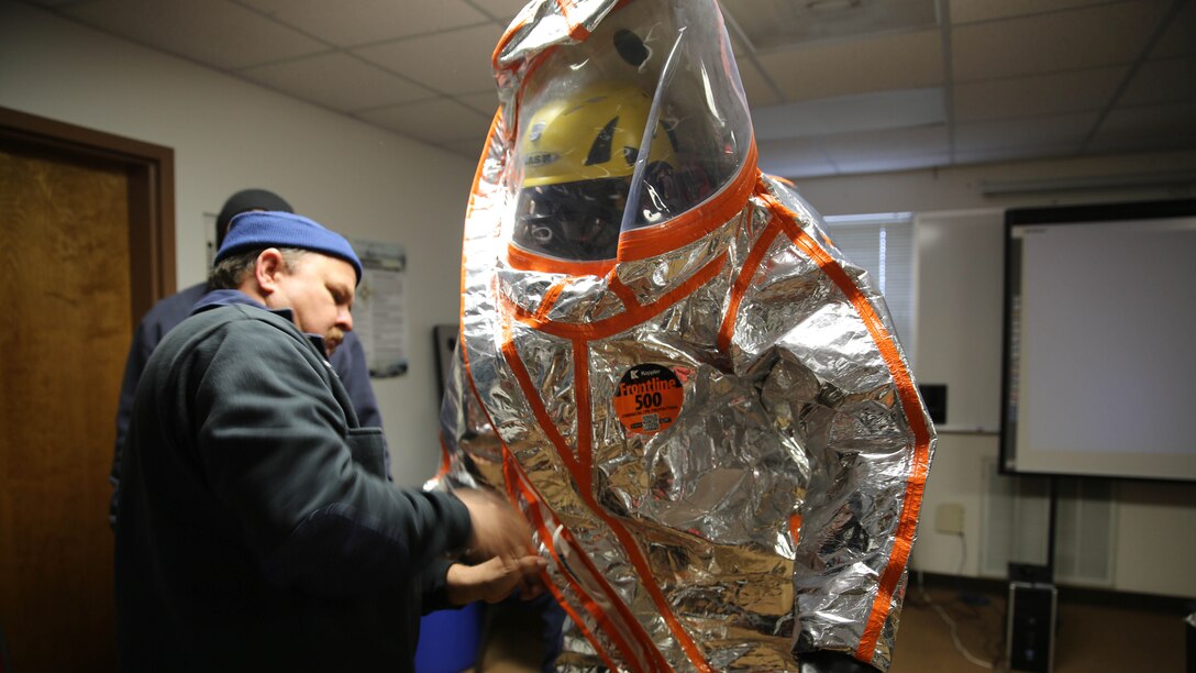 Ray Barnard, base firefighter, helps Layne Jackson, base firefighter and emergency medical technician, into protective gear used in hazardous waste emergency operations during a Hazardous Waste Operations and Emergency Response course aboard Marine Corps Air Station Beaufort, Jan. 14. The course, which is required for certain Marines and civilians the Air Station, has changes this year which reduce the cost from $600 to $1,000 per student to less than $50 per student.